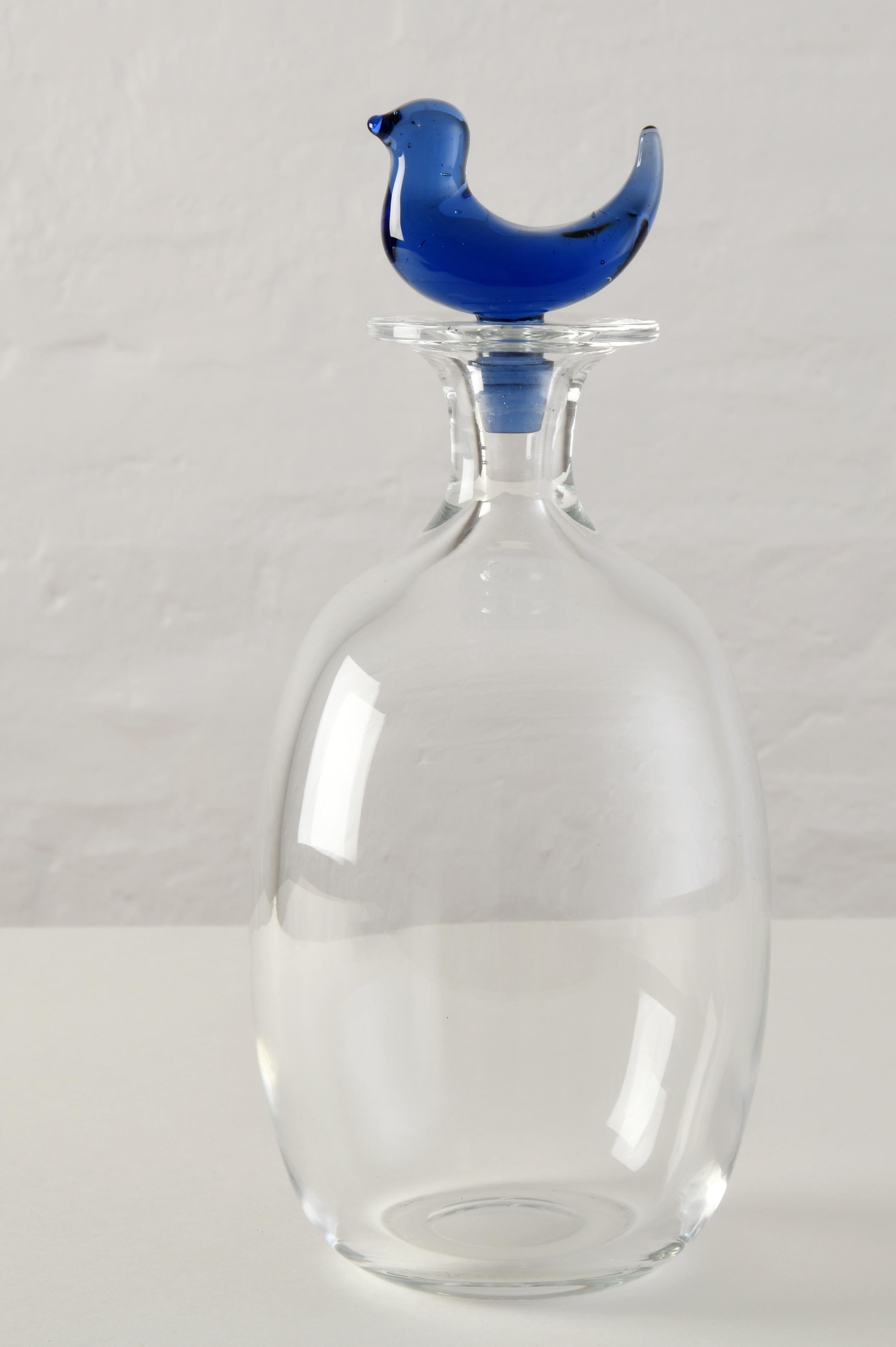 Glass carafe designed by Michael Bang in 1989 for the famous Danish glassware manufacturer Holmegaard. The carafe is made of clear, transparent glass, while the stopper at the top is made of blue-tinted glass and depicts a charming little stylised
