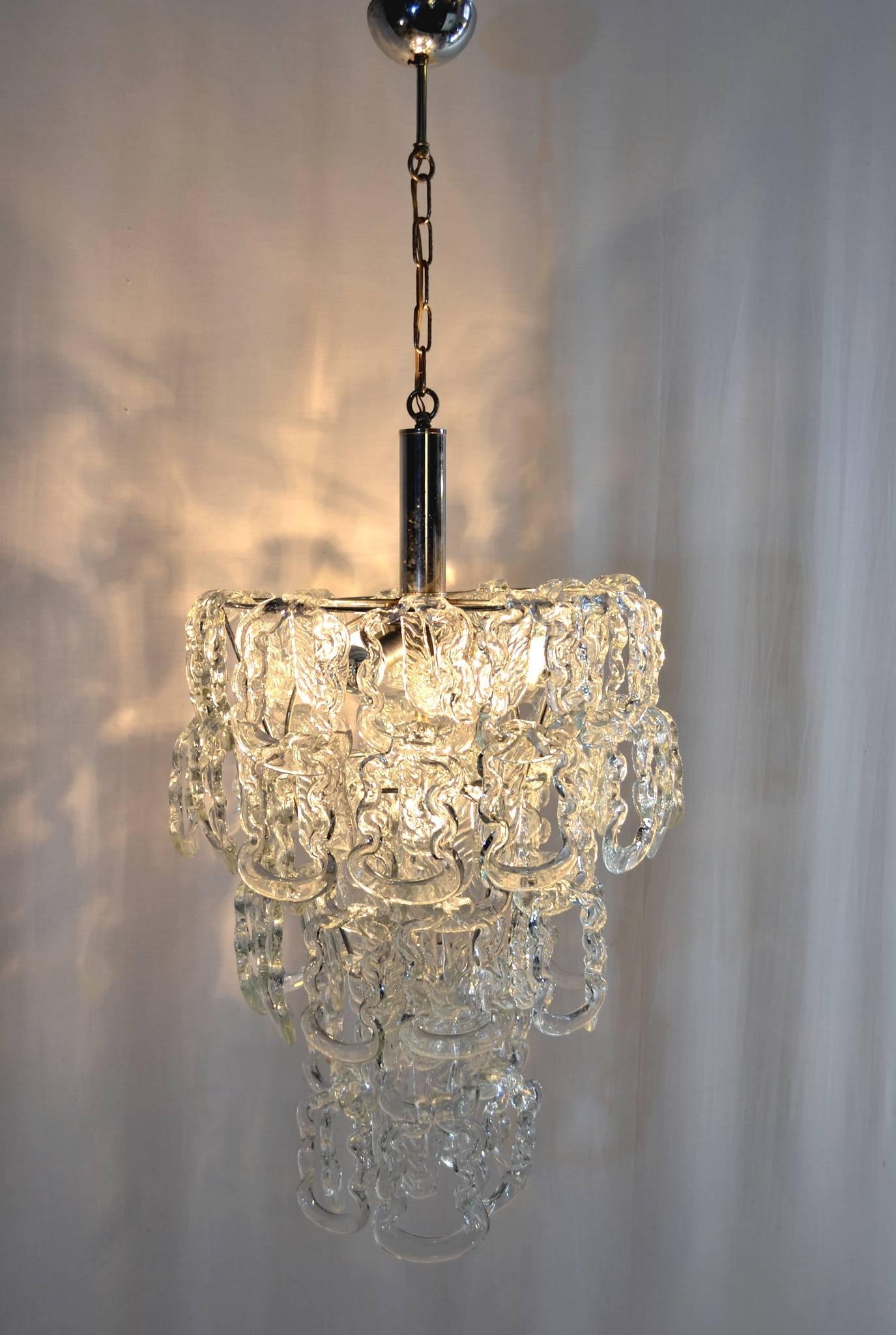 An original three tiered chandelier by Angelo Mangiarotti for Vistosi with Murano glass hanging from a chrome structure. The glass pieces can be hung a bit differently creating different heights for the chandelier. The height in this manner of the