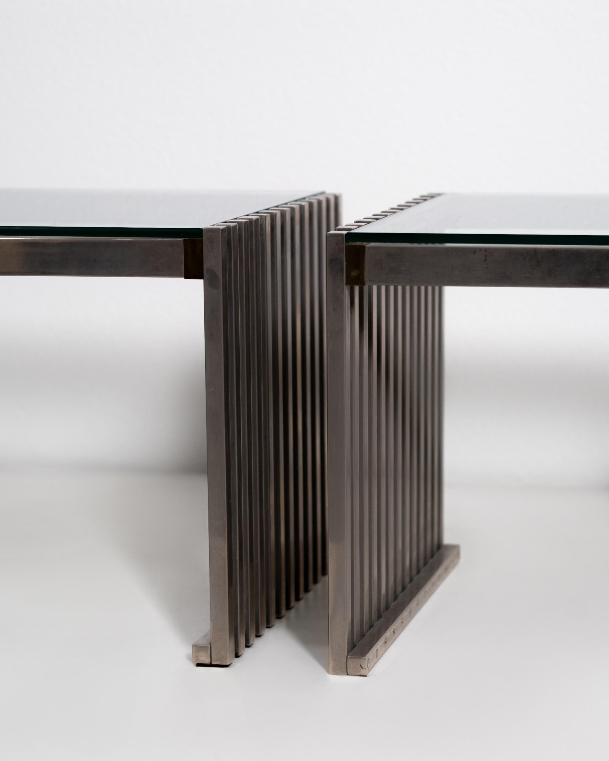 This elegant pair of glass coffee tables from the 1970s perfectly captures the minimalist ethos and refined material sensibility of mid-century modern design. Each table features a sturdy, polished steel frame with crisp, geometric lines, supporting