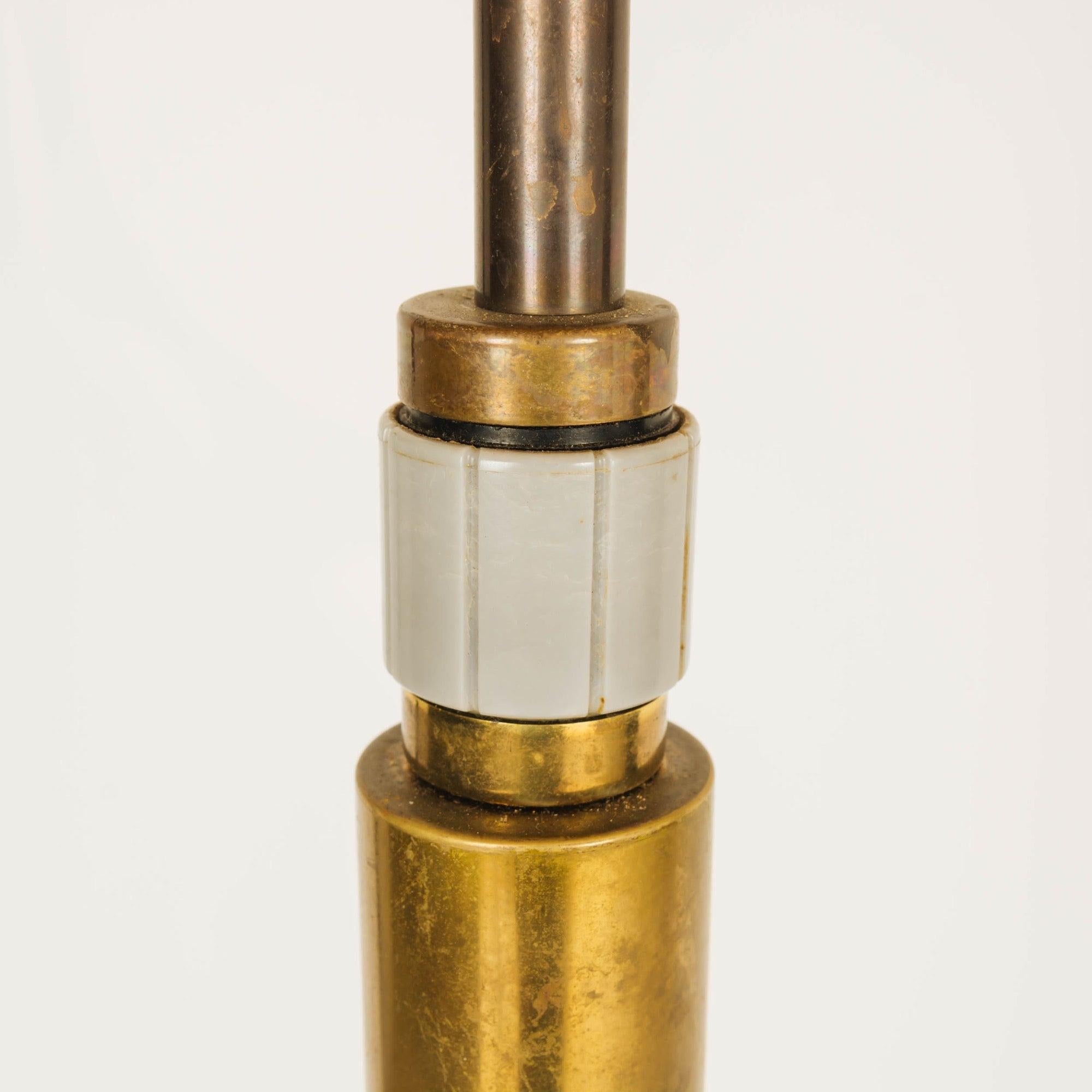 Una lampada da terra con una colonna cilindrica in vetro massiccio su una base quadrata arrotondata in ottone.