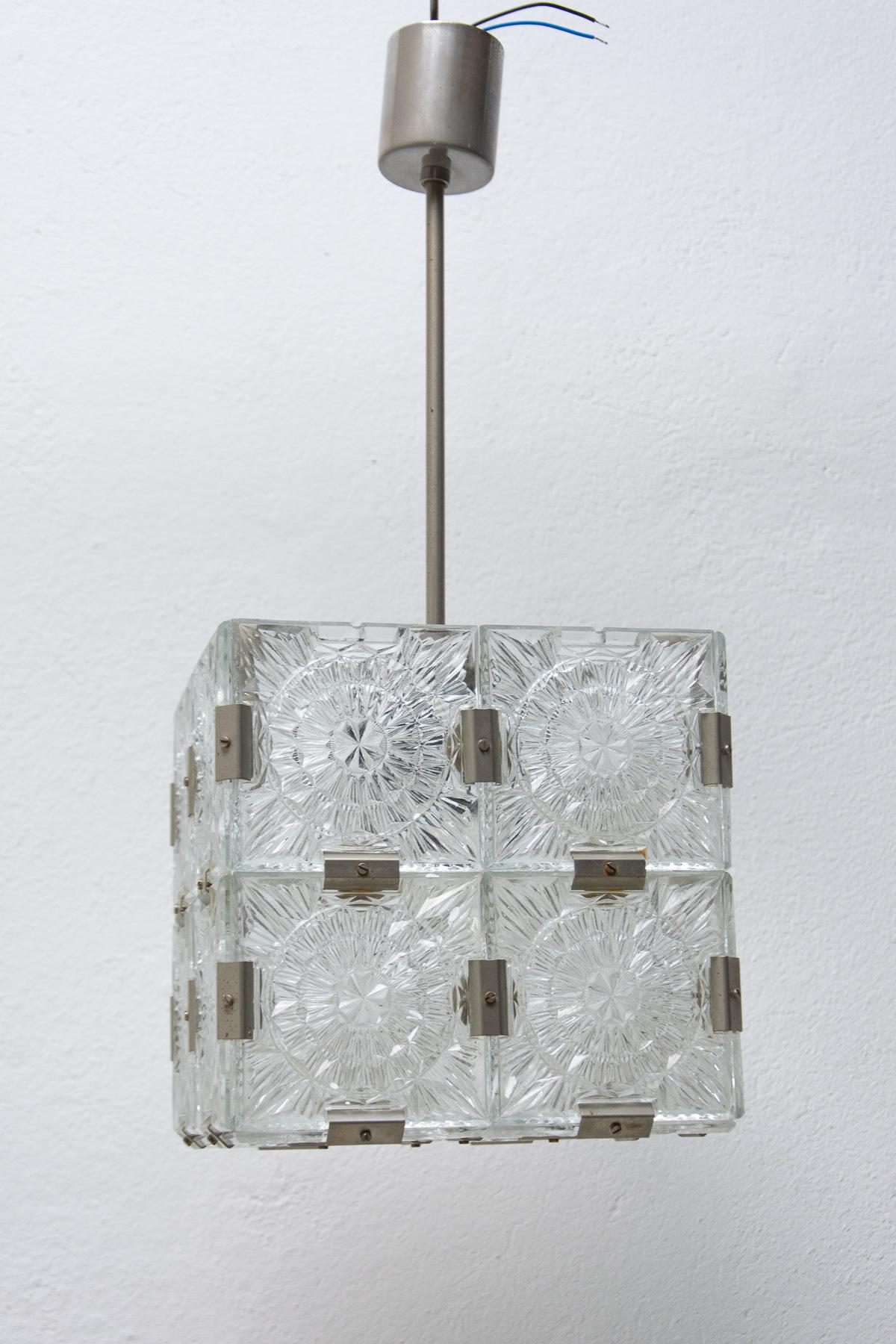 This glass cube hanging lamp was made by Kamenický Šenov company in the 1970’s. Made in the former Czechoslovakia.

Lamp is made of glass and metal. It´s composed of thick textured patterned square cut fetal pieces with chrome fittings. E27 bulb