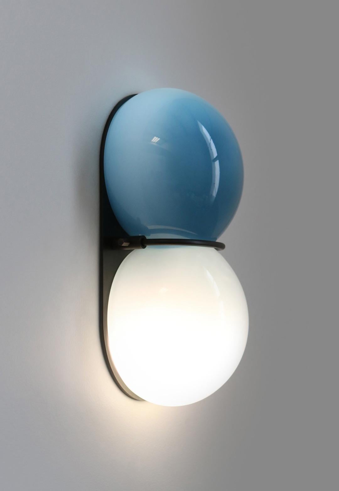 The Twin 1.0 Sconce features a two-tone diffuser of handblown Czech glass made up of two flattened spherical shapes in two colors which are melded together while hot on the glass blowing pipe. The glass is held to a solid brass plate canopy by a