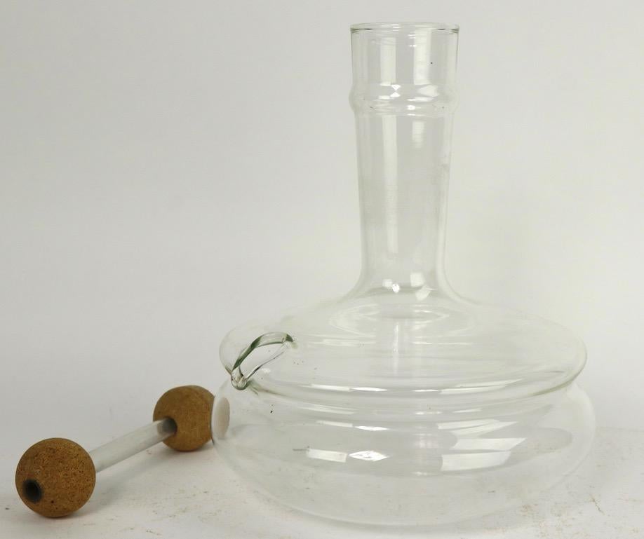 Stylish crystal decanter with cork barbell stopper. The decanter has an open top for filling the bottle, and a side mouth spout for pouring, the barbell form stopper has a glass tube center, and cork ball ends (one ball shows slight loss