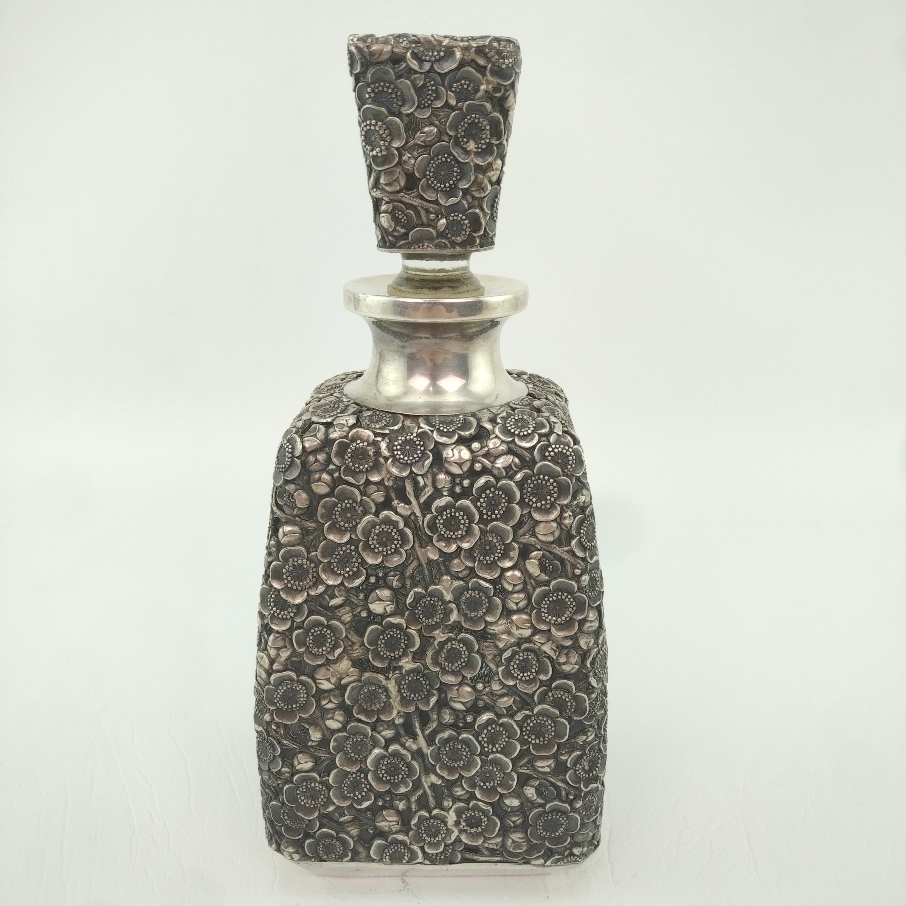 950 Fine Silver overlay decanter, circa 1930.

The silver overlay is a wonderful medley of flowers in repose work over a four sided pinched glass bottle, with a sterling silver overlay covered cork stopper.   Decanter is hallmarked Sterling 950, for