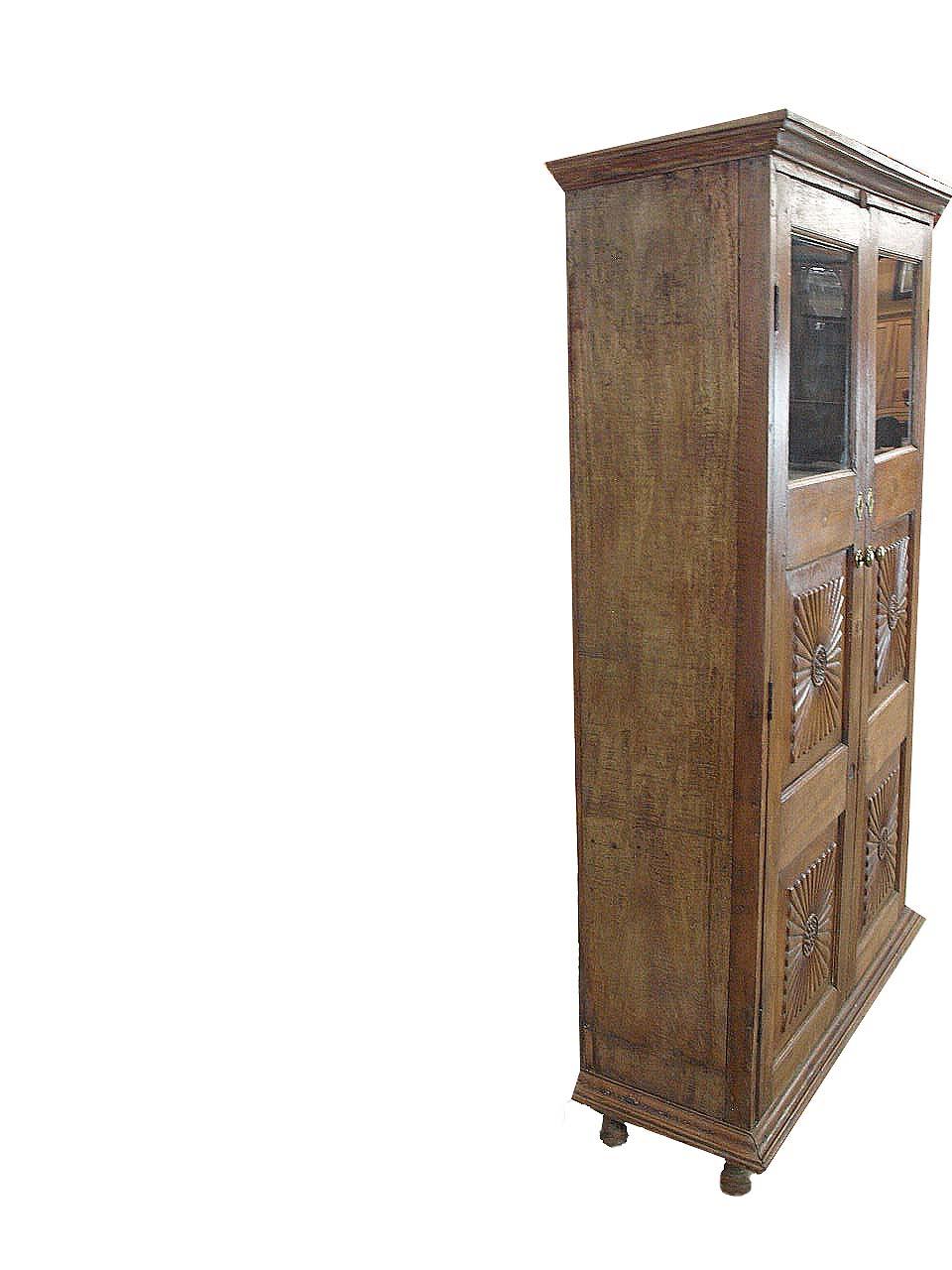 Glass door carved cupboard, with cove cornice above two doors with glass panels at the top and double carved panels below, interior with two shelves, resting on turned feet. It retains its original interior steel door latch.