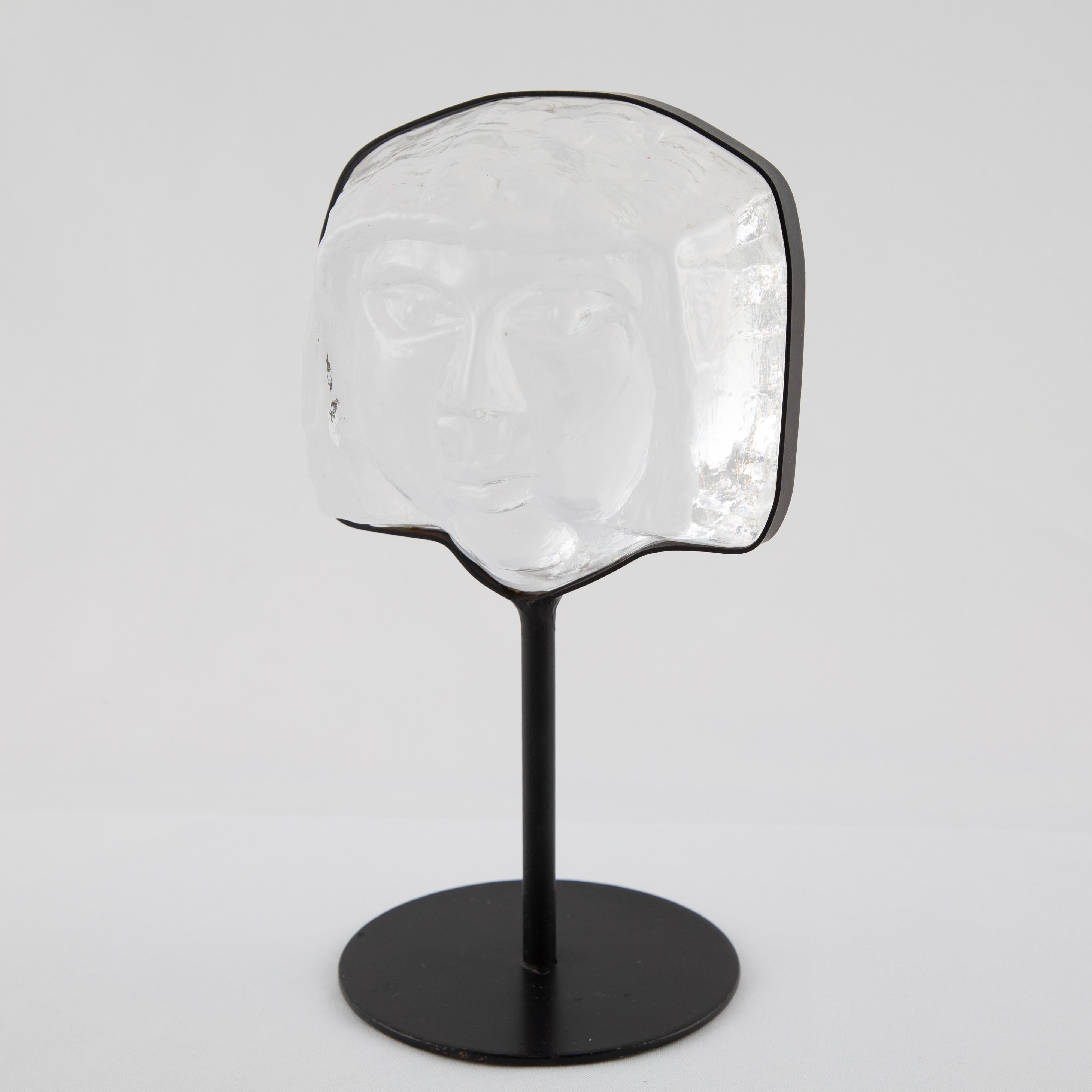 Thick, heavy art glass face sculpture supported by iron stand, by Erik Hoglund for Kosta Boda. Stamped 