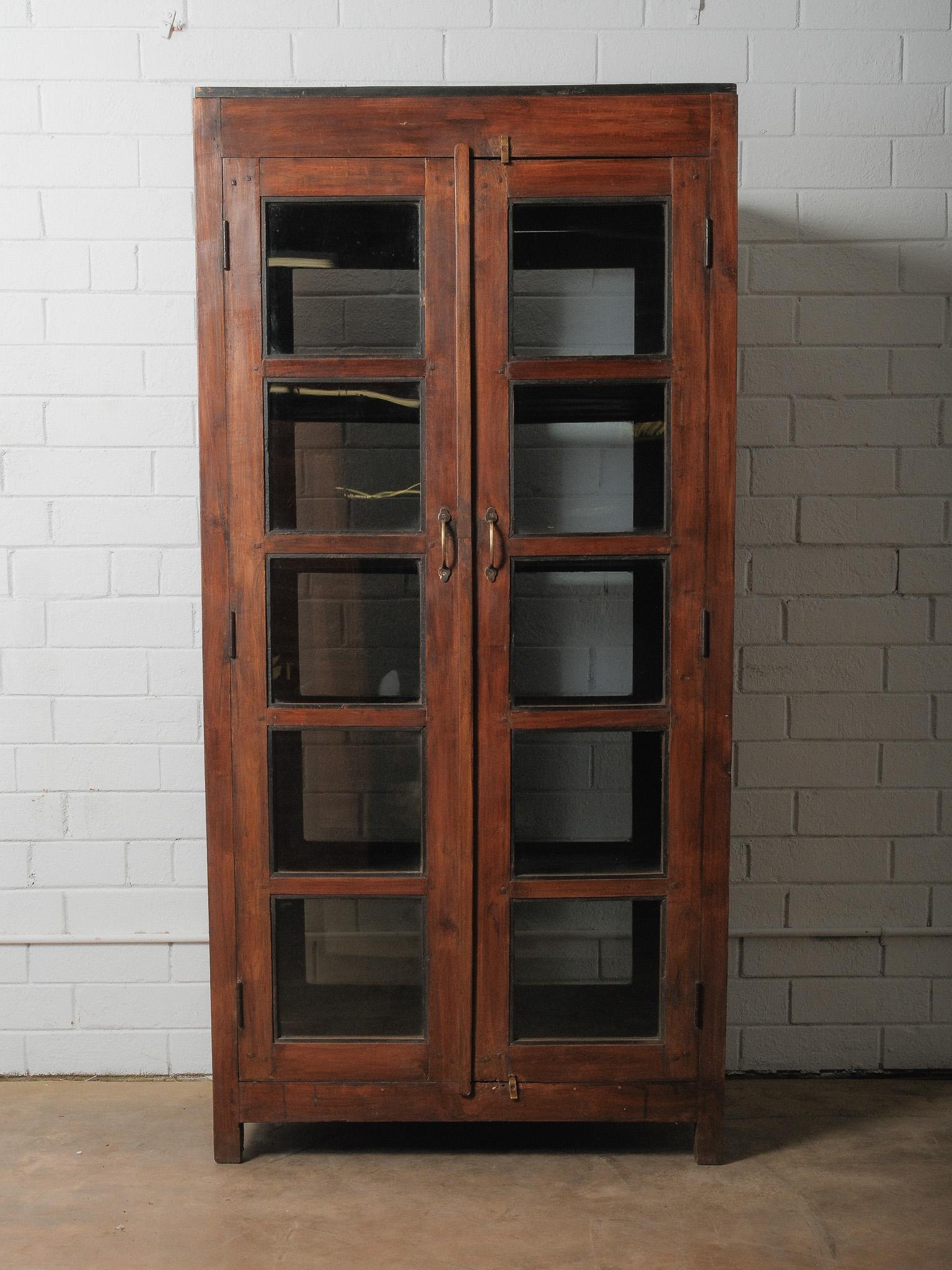 An object defined by symmetry and intention, this dual-sided glass cabinet carries an understated architectural presence. Crafted in warm, richly toned wood, the cabinet opens from both front and back—an uncommon and beautifully functional detail