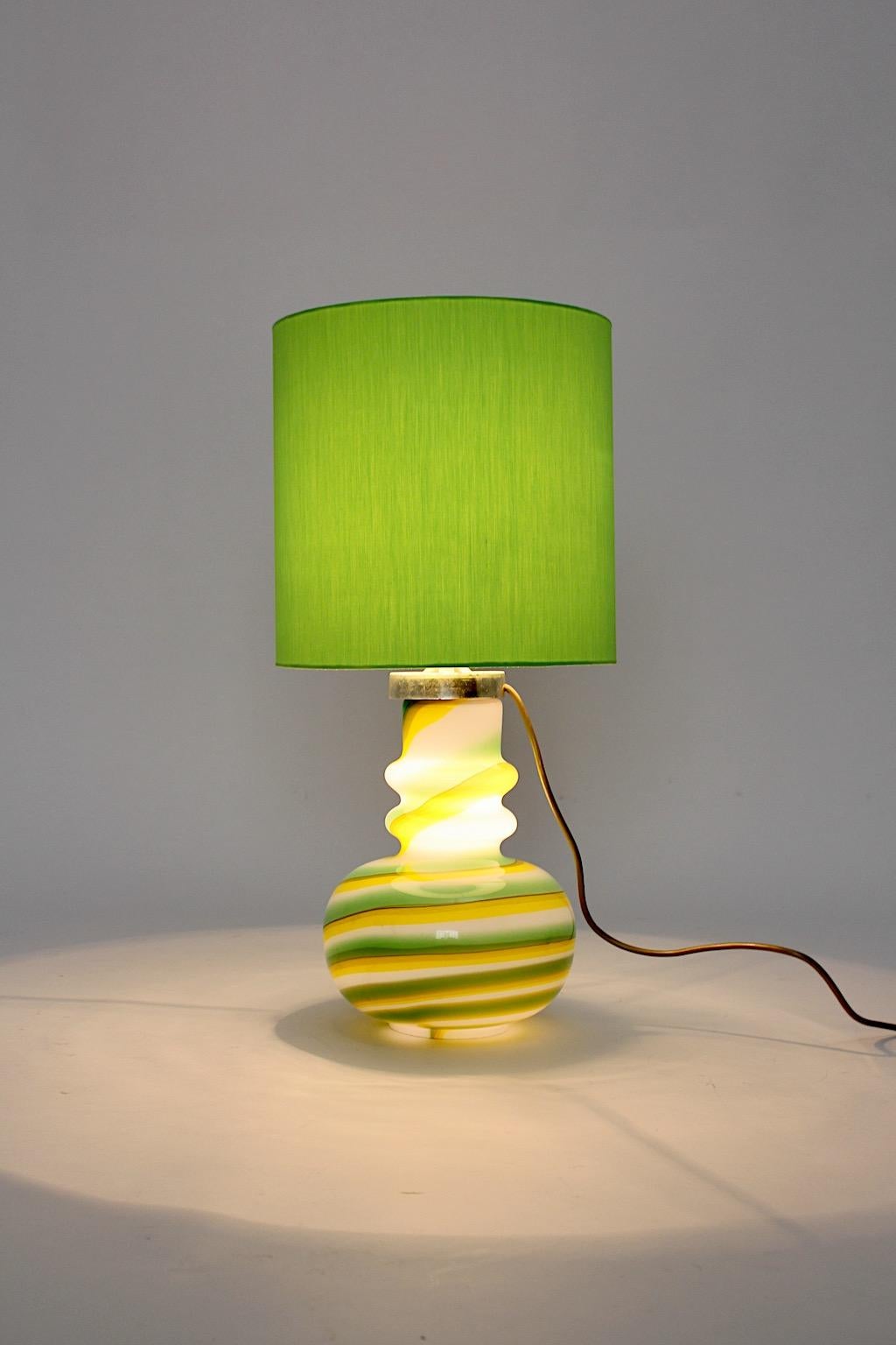 Space Age vintage table lamp from glass in happy colors green, yellow and white designed and executed, Italy, 1960s.
While the striped glass body shows a beautiful shape, the grass green lamp shade is renewed.
Two E 27 sockets and on/off switch at