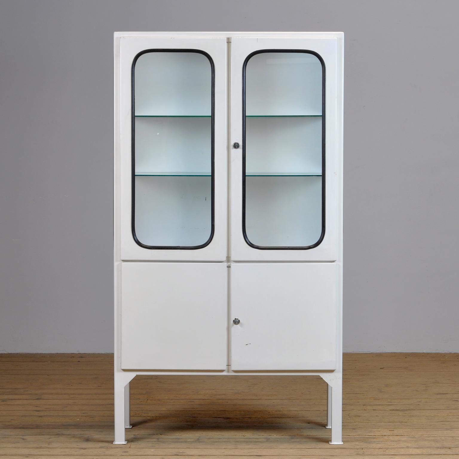 This medicine cabinet was designed in the 1970s and was produced circa 1975 in hungary. It is made from iron and glass, and the glass is held by a black rubber strip. The cabinet features two adjustable glass shelves and functioning locks.
