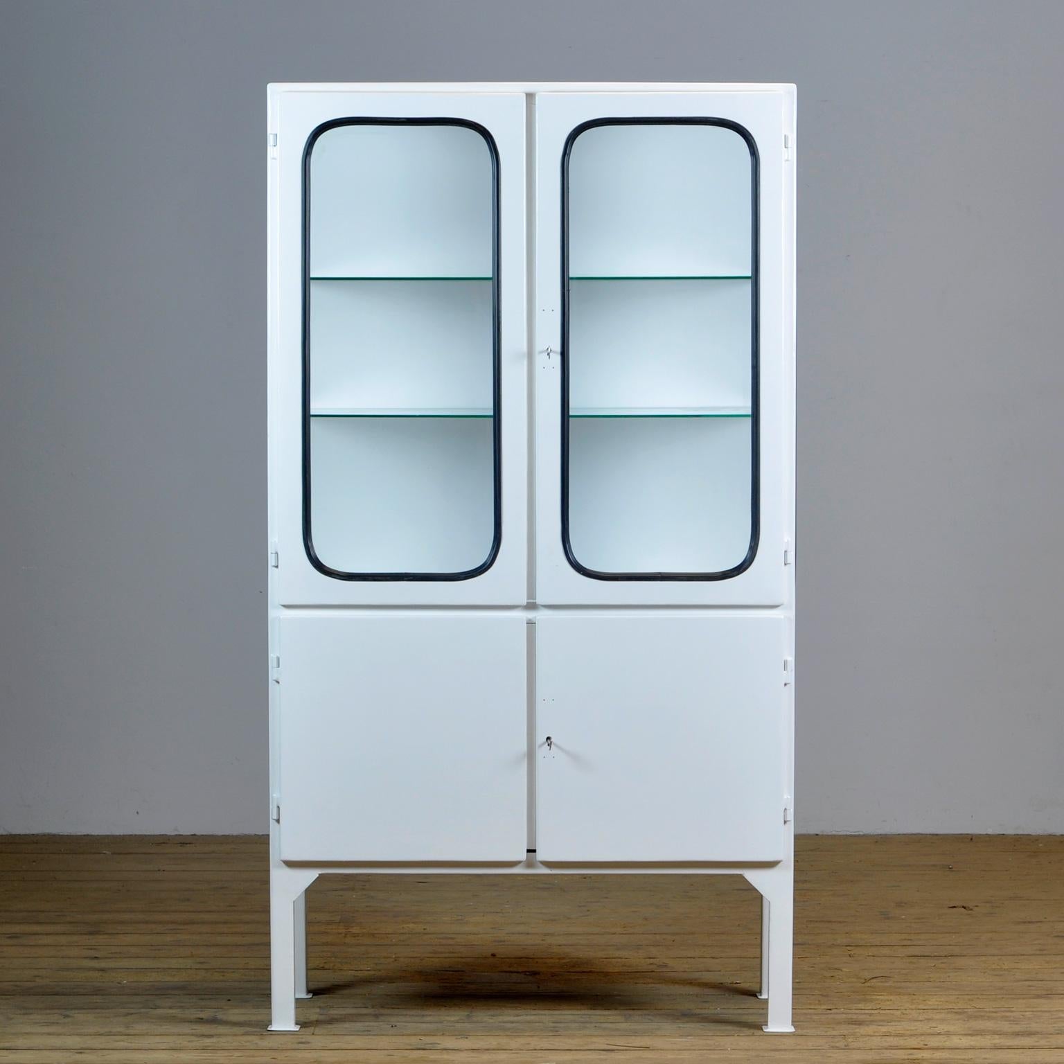 This medical cabinet was designed in the 1970s and was produced circa 1975 in hungary. It is made from iron and glass, and the glass is held by a black rubber strip. The cabinet features two adjustable glass shelves and functioning locks.