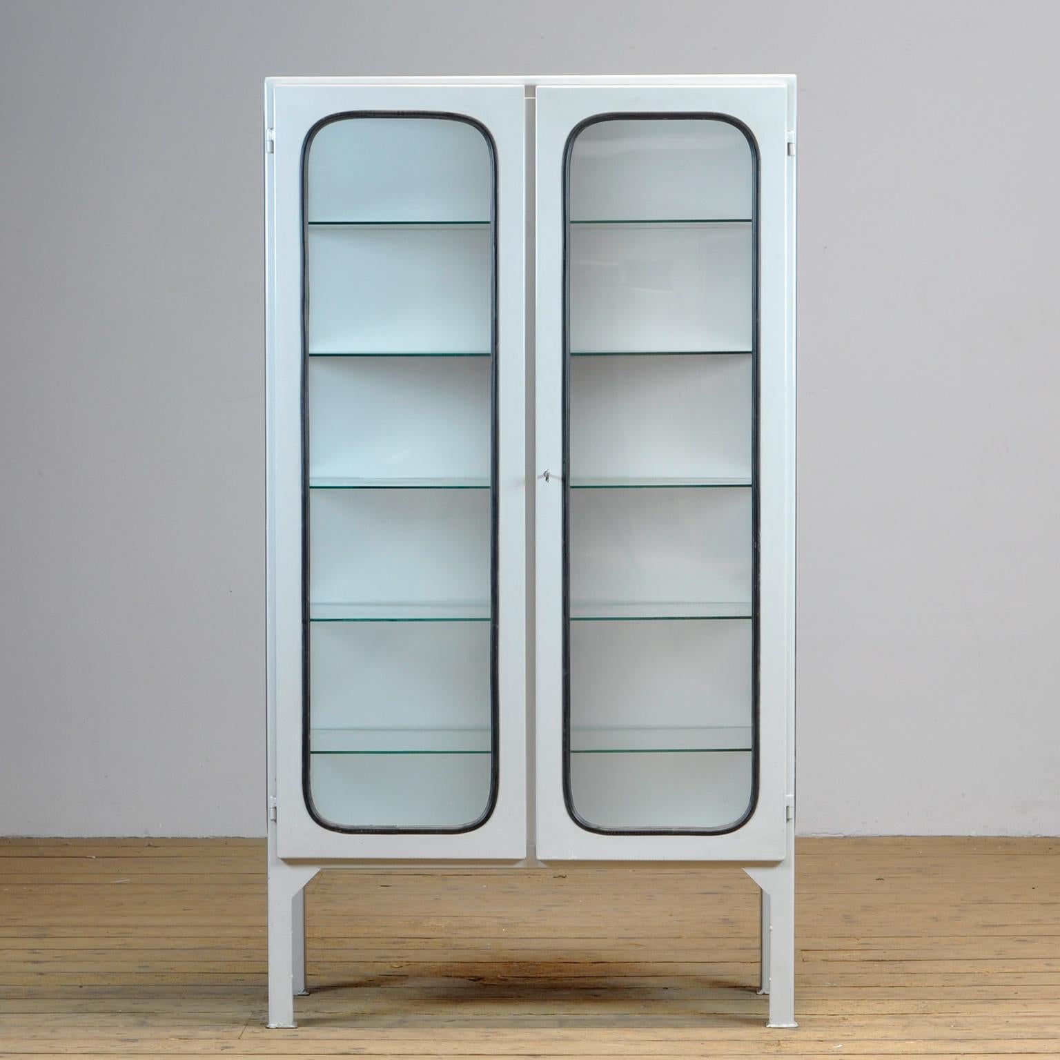 This medical cabinet was designed in the 1970s and was produced circa 1975 in hungary. It is made from iron and glass, and the glass is held by a black rubber strip. The cabinet features five adjustable glass shelves and a functioning lock. 
