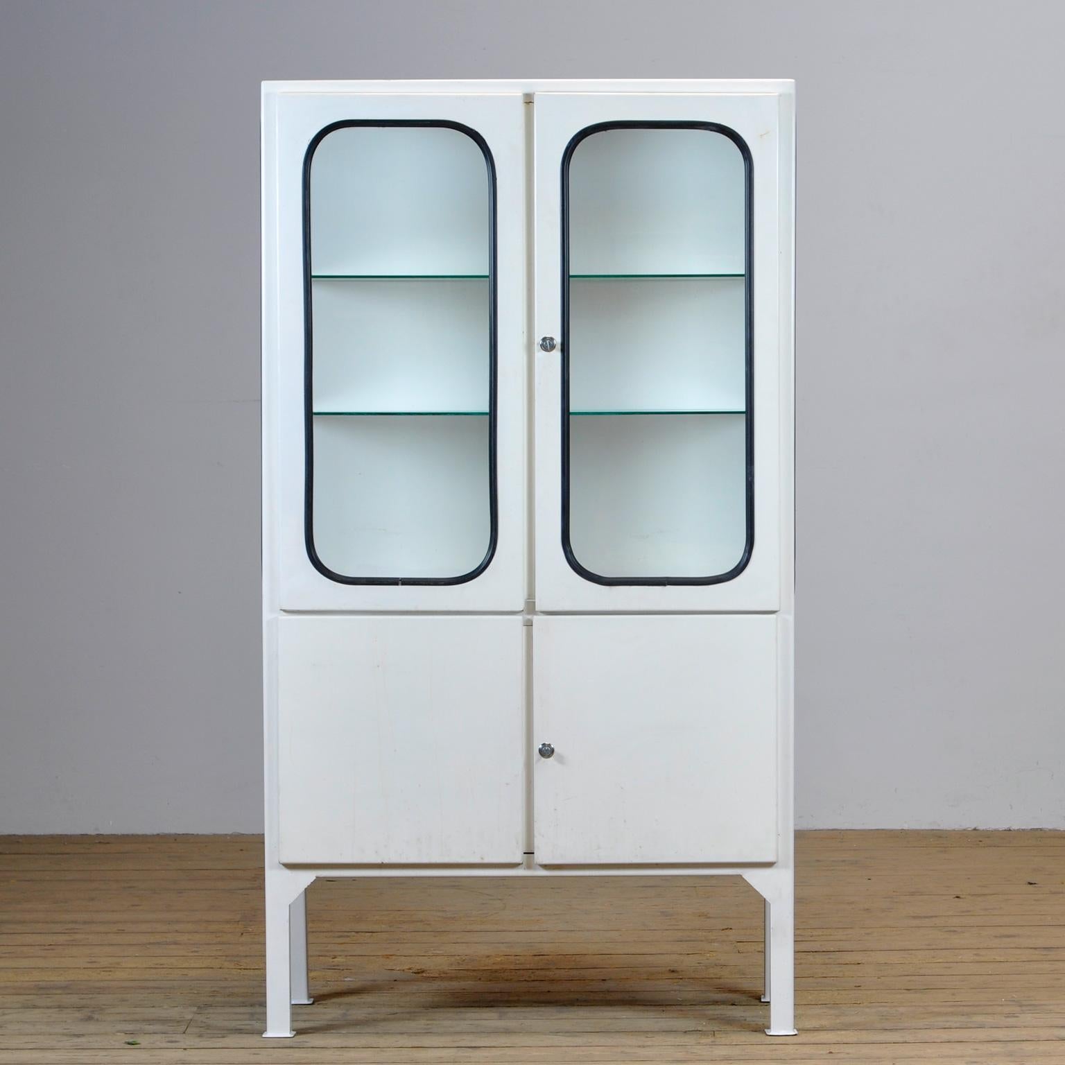 This medical cabinet was designed in the 1970s and was produced circa 1975 in Hungary. It is made from iron and glass, and the glass is held by a black rubber strip. The cabinet features two adjustable glass shelves and functioning locks. 