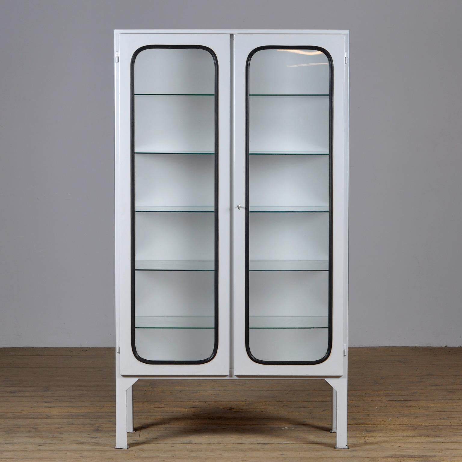 This medical cabinet was designed in the 1970s and was produced circa 1975 in hungary. It is made from iron and glass, and the glass is held by a black rubber strip. The cabinet features five adjustable glass shelves and a functioning lock. 
