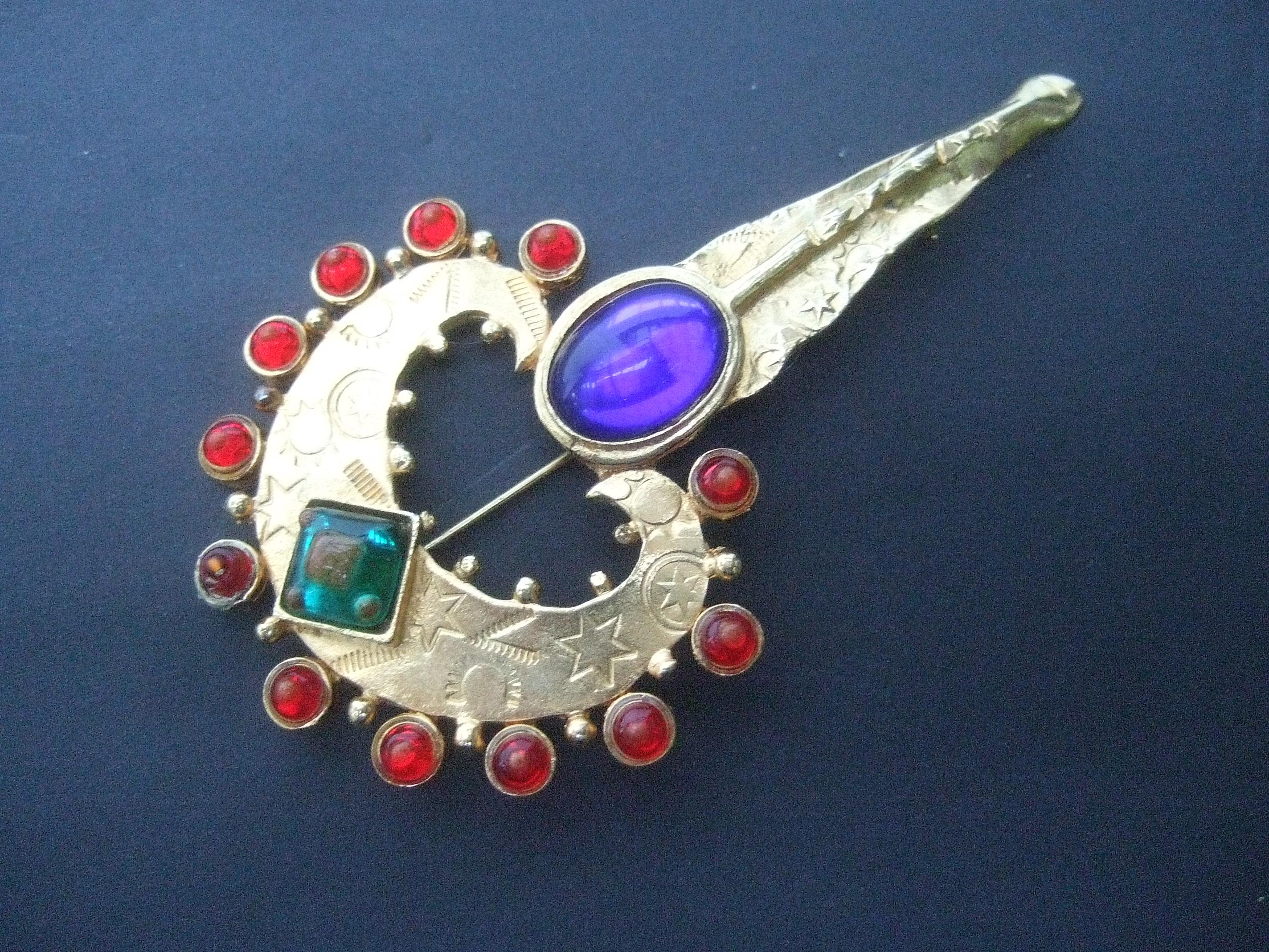 Ornate glass jeweled heart & key brooch designed by Robert Rose
The large scale gilt metal brooch is embellished with a collection of glass settings in a myriad of colors

The rounded heart is framed with a band of red glass cabochons. The center of