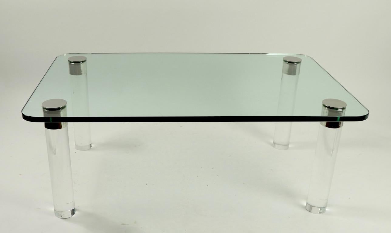 Chic and stylish glass top coffee table having cylindrical Lucite legs, with chrome disk tops. The table is in very good original condition showing only light cosmetic wear normal and consistent with age. Thick rectangular plate glass top ( .75 in.