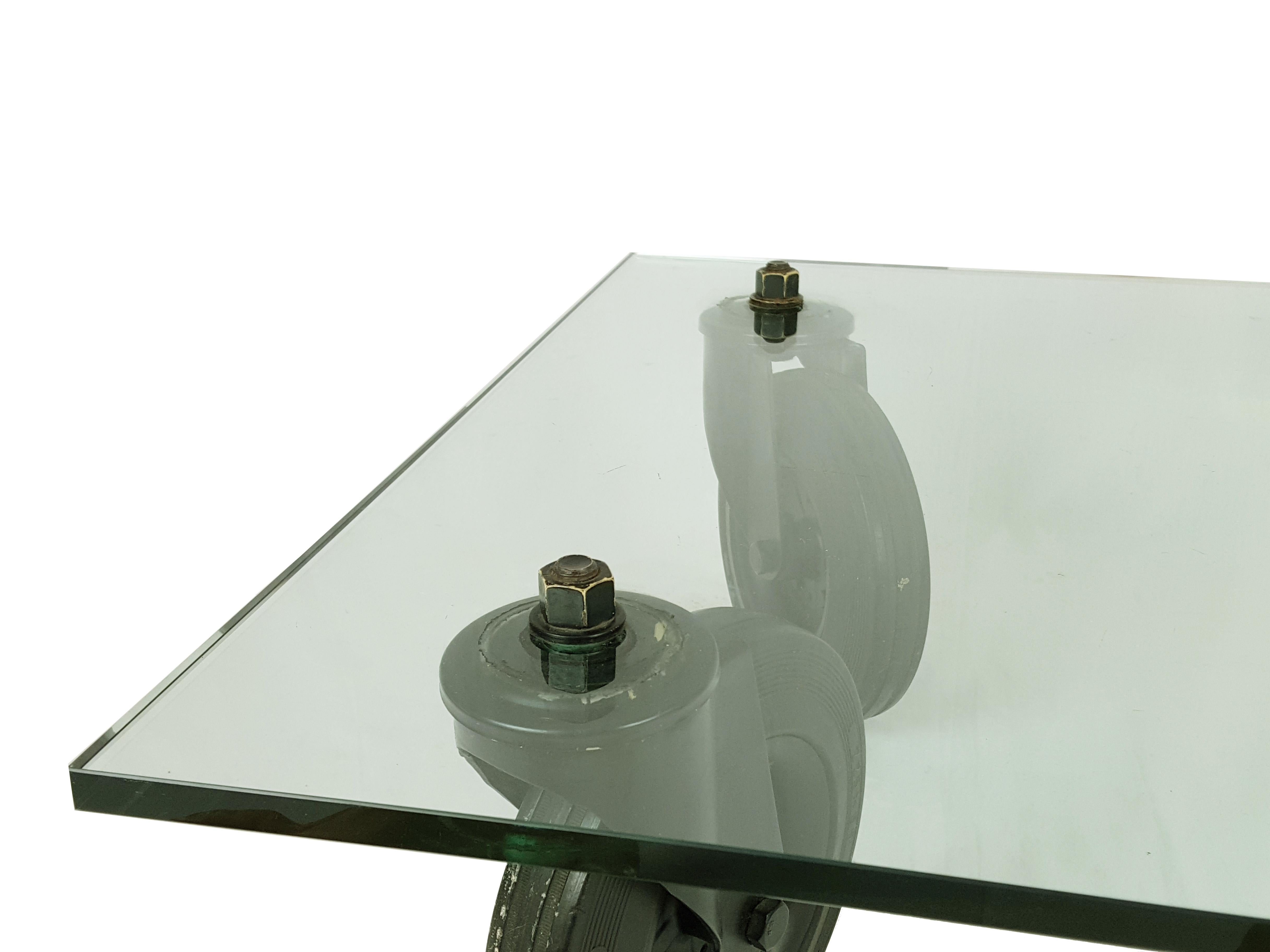 Tavolo basso in vetro tagliato spesso e ruote industriali disegnato in varie dimensioni da Gae Aulenti per Fontana Arte negli anni '80. Il tavolo è in buone condizioni, con leggerissimi difetti sul vetro. Non presenta segni di produzione.