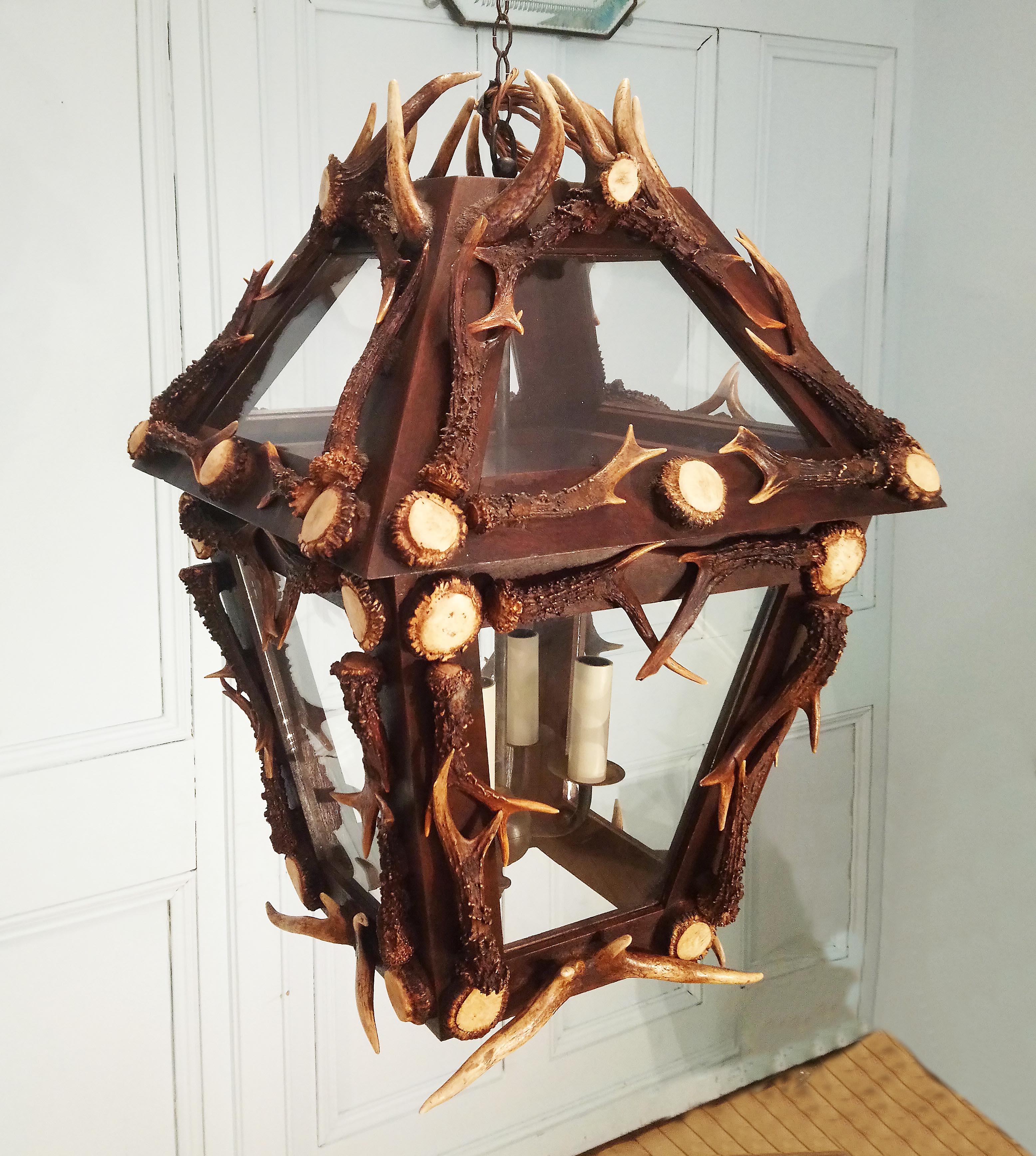 This striking and unique rustic style lantern is designed from naturally shed antler horn from red deer in Scotland. The lantern features eight glass panels set in a mahogany frame and four candle shaped light fittings. The light measures 17 in –