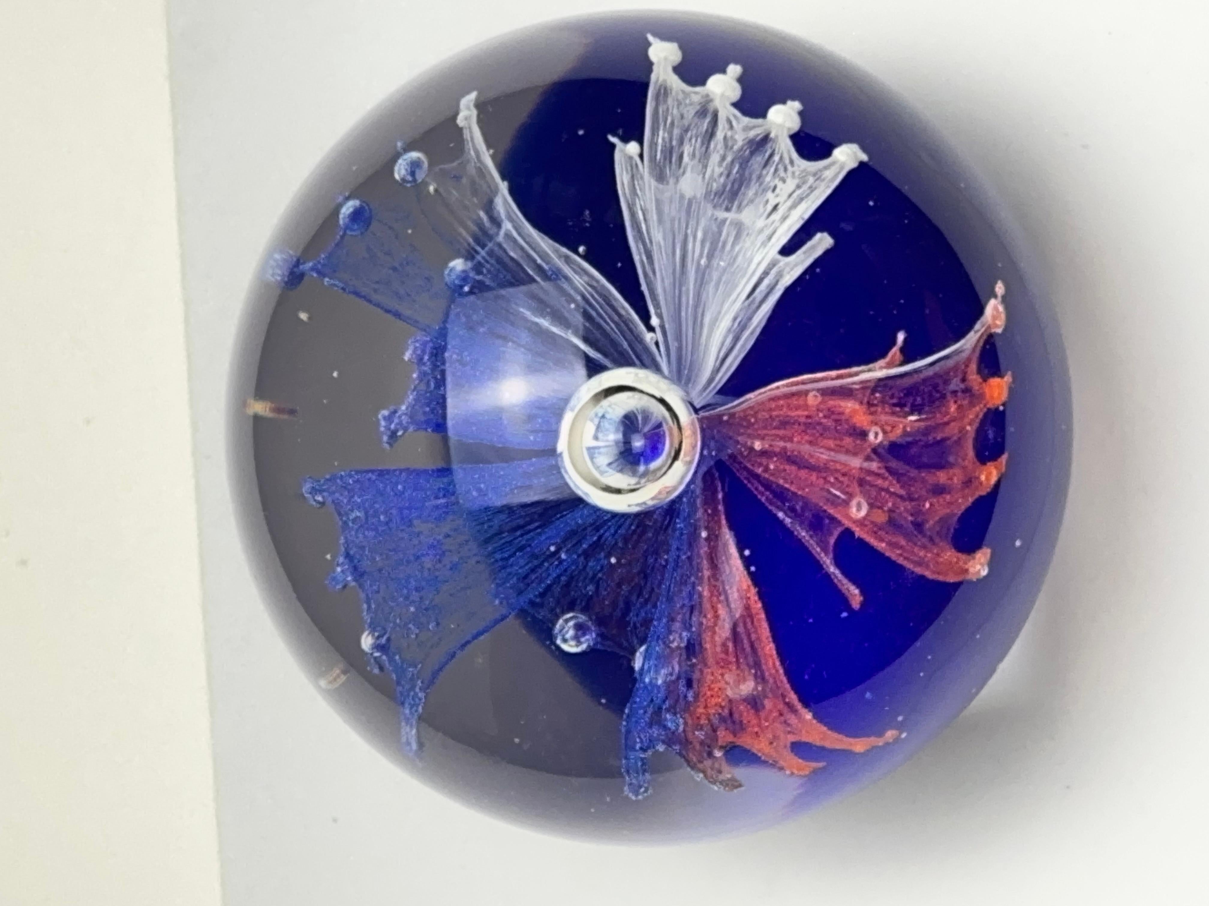 A vintage 1980s red, white, and blue glass paperweight of spherical form.

It’s an intriguing piece of art-glass, that showcases exceptional skill and technique; the kind that can only be achieved by fine glassmaking artisans.

The central display