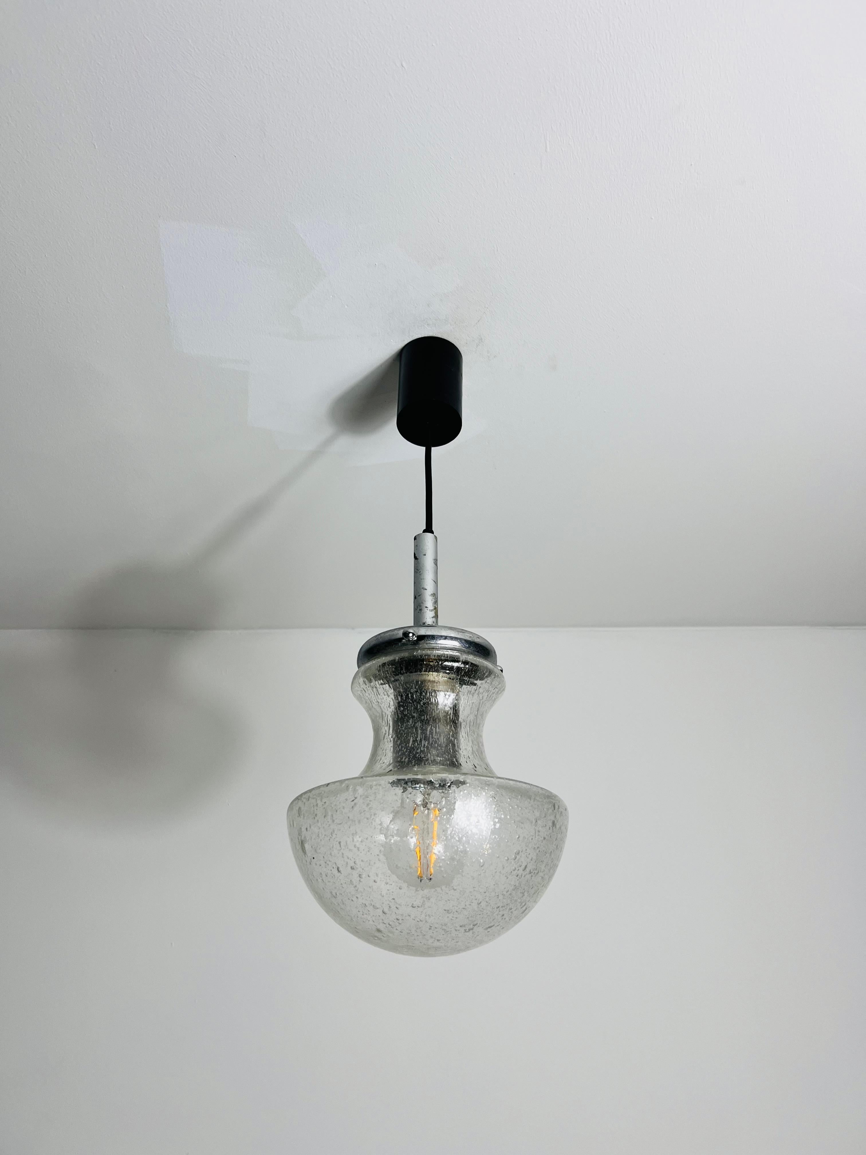 A stunning glass hanging lamp made in Germany in the 1970s. This elegant light fixture features exquisite Murano glass, known for its superior quality and craftsmanship. The glass is beautifully textured with wave and bubble patterns, giving it a