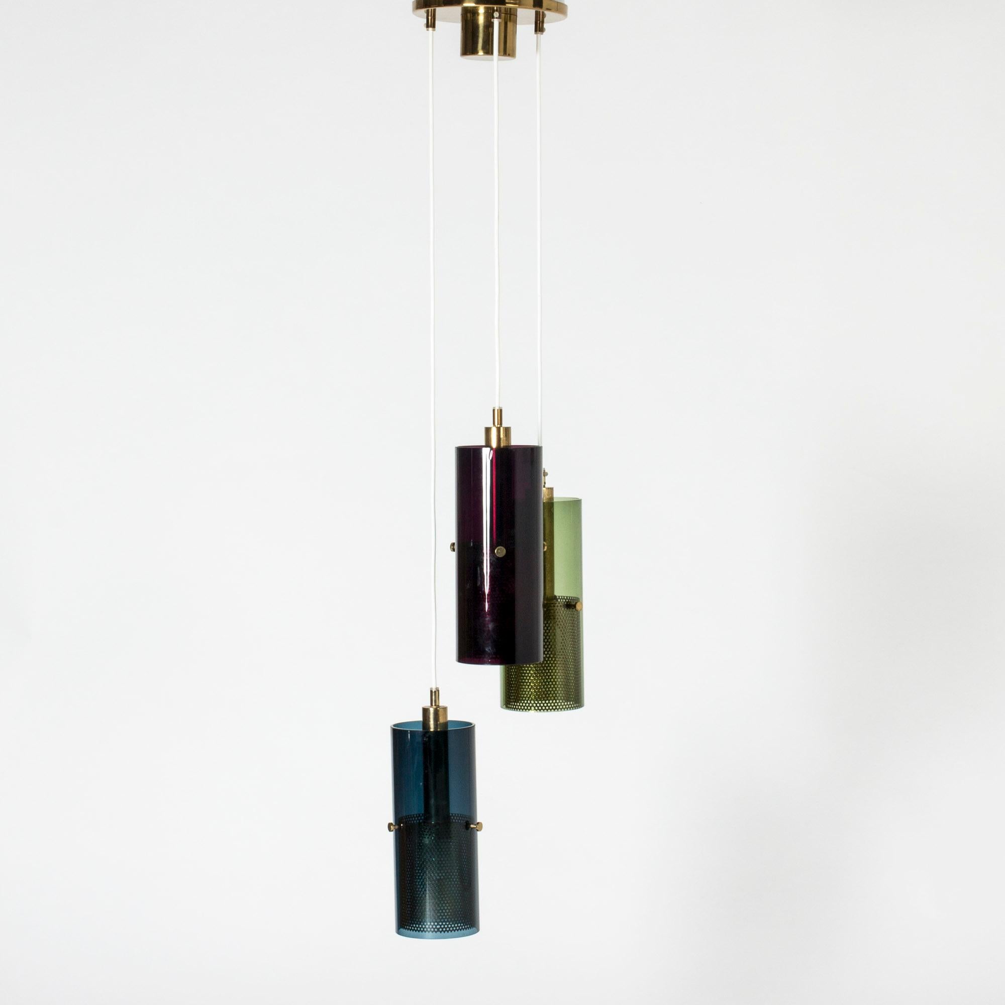 Auffällige Deckenleuchte von Hans-Agne Jakobsson mit drei zylindrischen Glasschirmen, die an einem großen Messingdeckenbecher hängen. Perforierte Messingzylinder im Inneren umschließen die Lichtquellen und lassen das rote, blaue und grüne Glas in