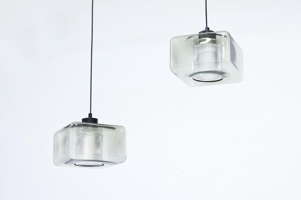 Square shaped glass pendant lamps
designed by Carl Fagerlund. Made
by Orrefors in Sweden during the
1960s. Light grey tinted glass outer
cup with a cylinder internal diffuser
in clear pressed glass. Rewired.