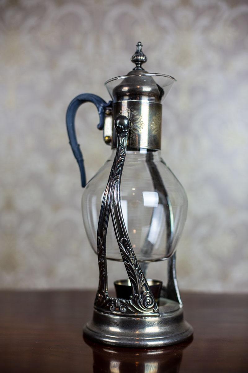 We present you a pitcher on a stand, with a heater manufactured by the Gorham Company in Newport, USA in the 1930s.
The stand, the pitcher neck and lid are made of silver plated metal.

Capacity: 1.5L.

This item is in perfect