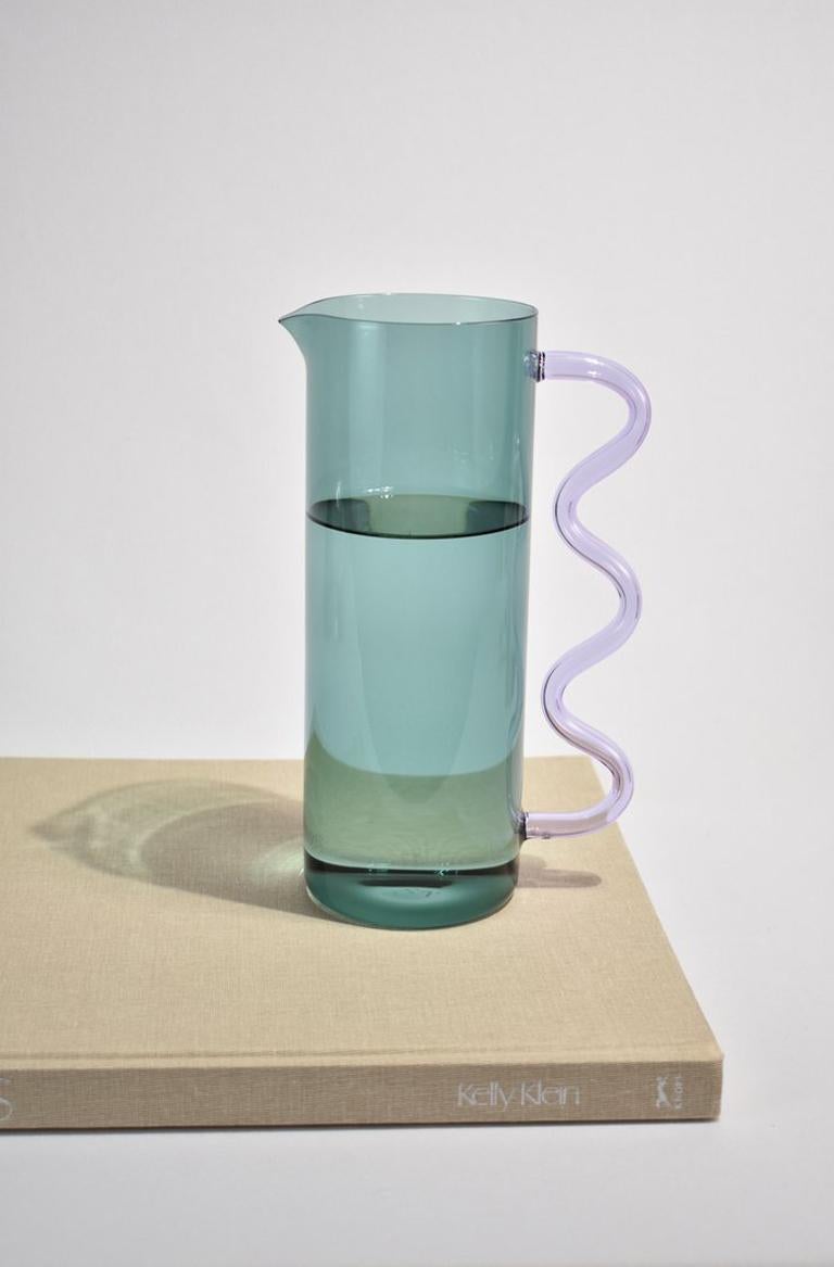 Glass pitcher in teal with a lilac wavy handle. May be used for holding flowers, watering plants, a pitcher for juice or any other use you can think of. Designed by Sophie Lou Jacobsen in New York. Made of lightweight and durable borosilicate glass.