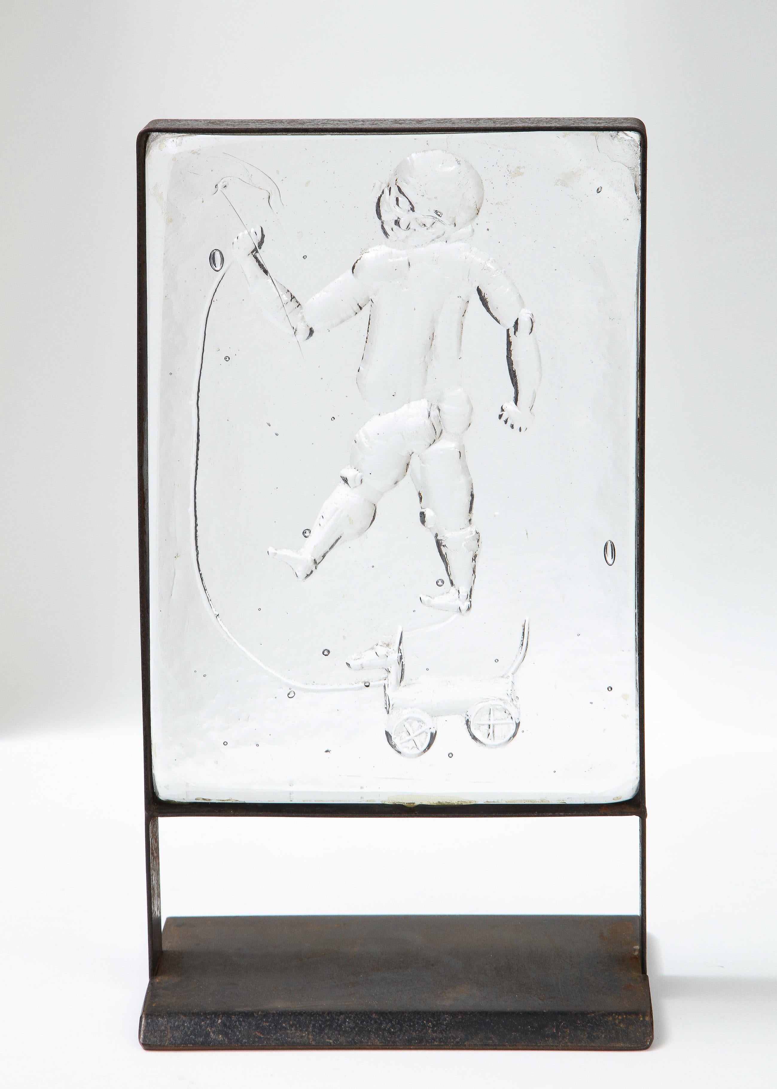 Escultura en relieve de cristal de un niño, obra de Erik Hoglund para Kosta Boda, insertada en un marco de acero de pie.
