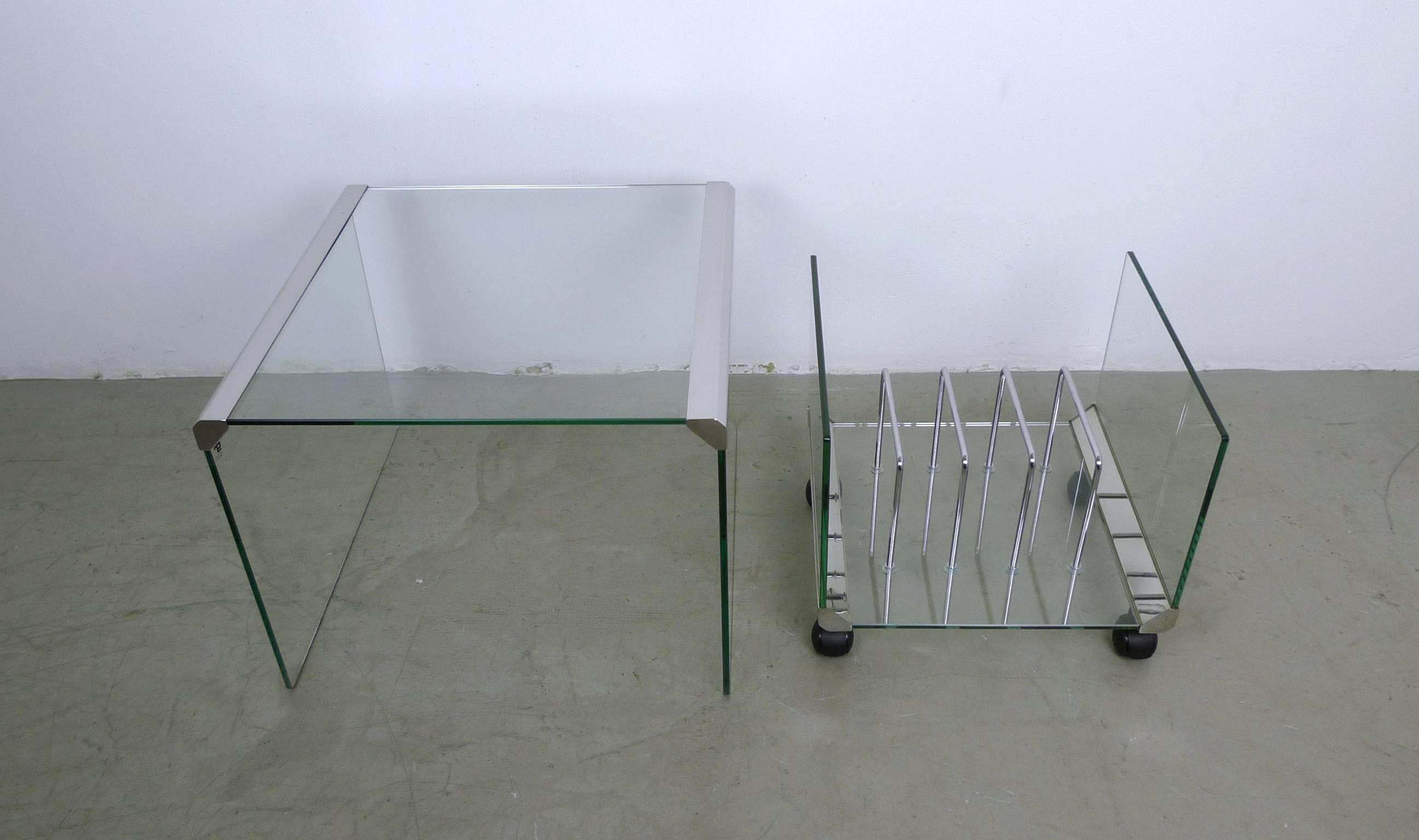 This square side table made of glass features veneered metal edges and a matching magazine rack on castors. The magazine rack measures 42 cm wide, 40 cm deep and 36 cm high. The side table measures can seen below.
This set was produced in the 1970s