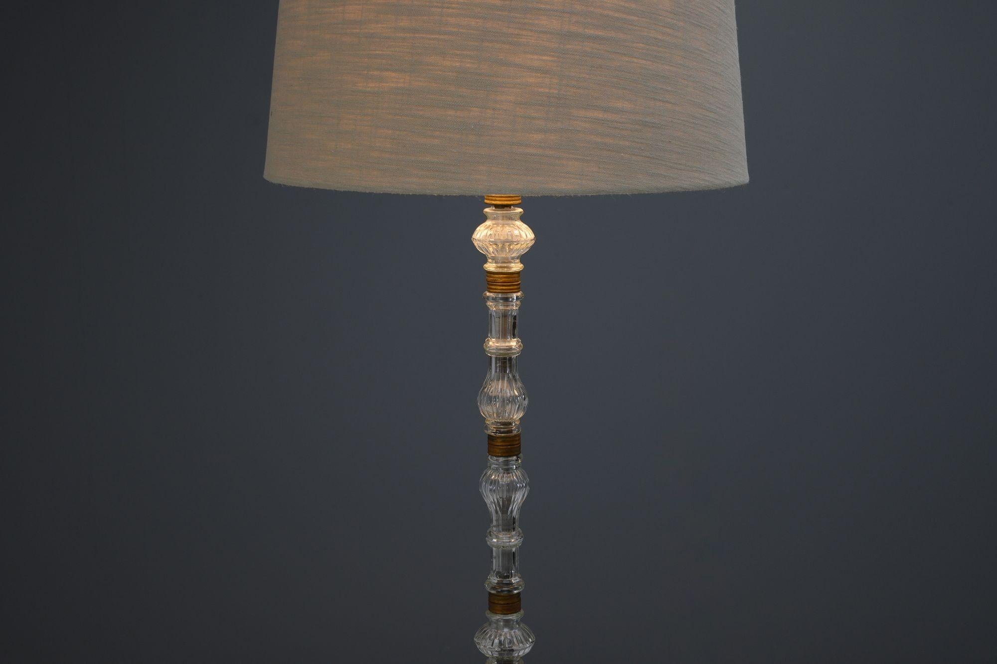 Lampadaire à tige en verre sur base en métal forgé. L'abat-jour n'est pas inclus. Circa 1930.
H 169cm x L 39cm x P 39cm
