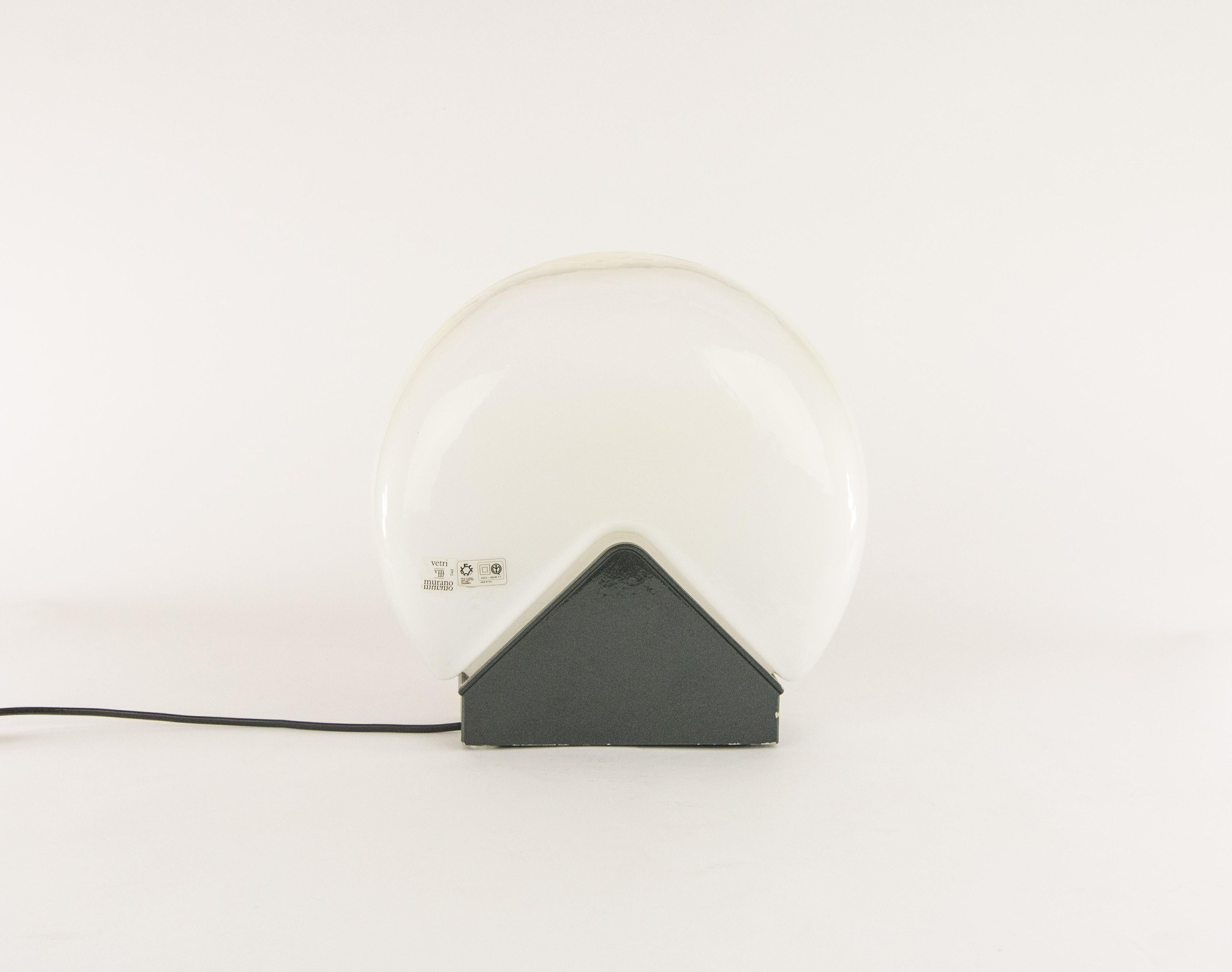 Lampe de table élégante de Roberto Pamio pour le fabricant italien de luminaires en verre Leucos.

Un beau capuchon demi-rond en verre fait main posé sur une base en métal. Le verre est blanc sur le fond et va jusqu'à être complètement