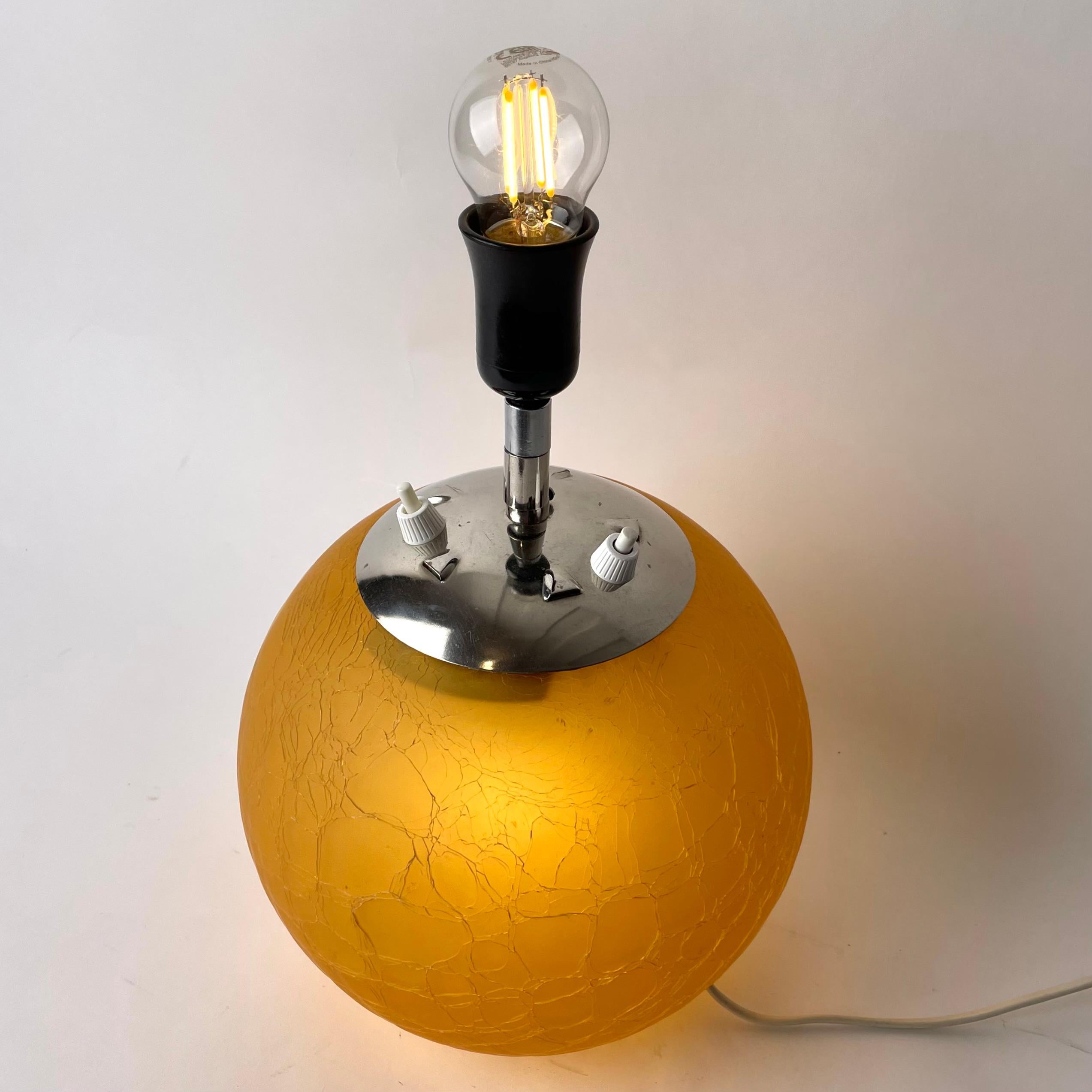 Glass Table Lamp with elegant double lighting, one lamp in the visible lampholder and another lamp inside the glass ball. Period Art Deco made during the 1930s in a cracked glass so-called ”Skansen Glass” (Swedish) and with a top in chrome.

Wear