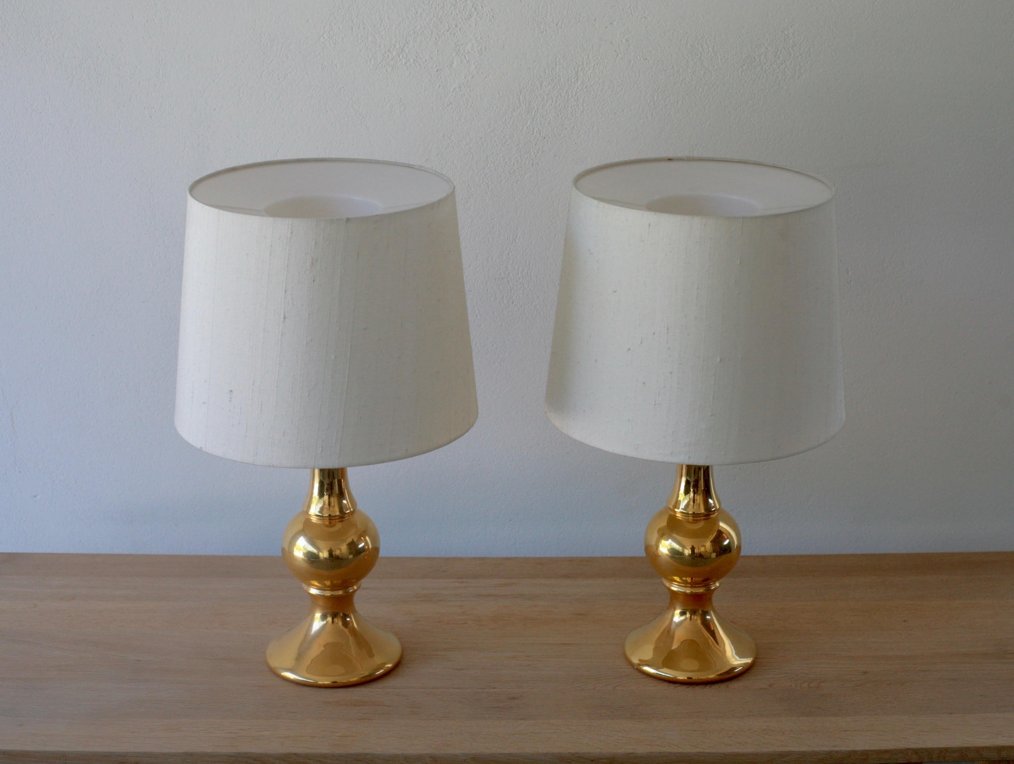A pair of gilded glass table lamps designed by Swedish design brothers Uno & Östen Kristansson. Lamp feet made by Flygsfors glass factory in Sweden and the lamps assembled by Kristiansson´s own factory Luxus in Vittsjö, Sweden. Original linen shades.