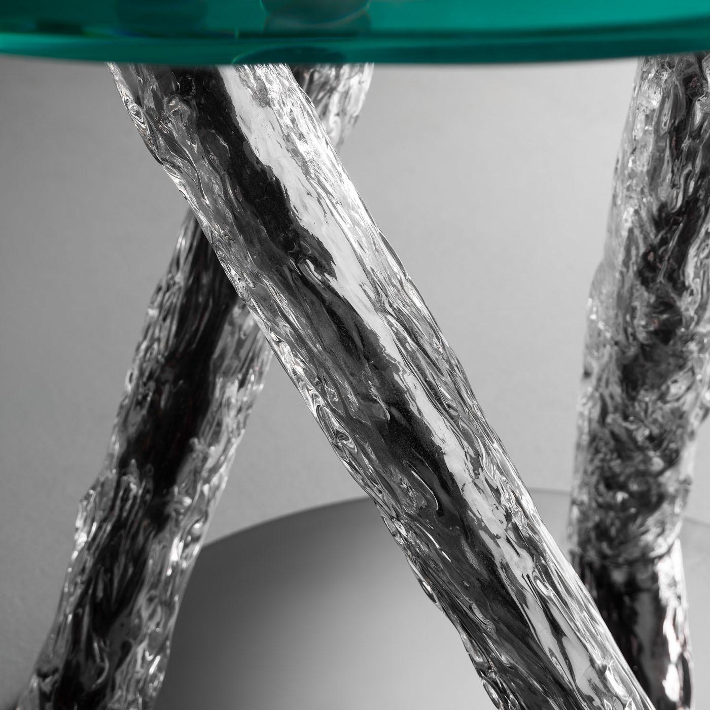 Cette table d'appoint sculpturale est une maîtrise du design, mêlant confort et élégance dans une sublime harmonie. Le plateau circulaire en verre est ancré par une colonne unique composée de trois tiges métalliques qui se tordent et