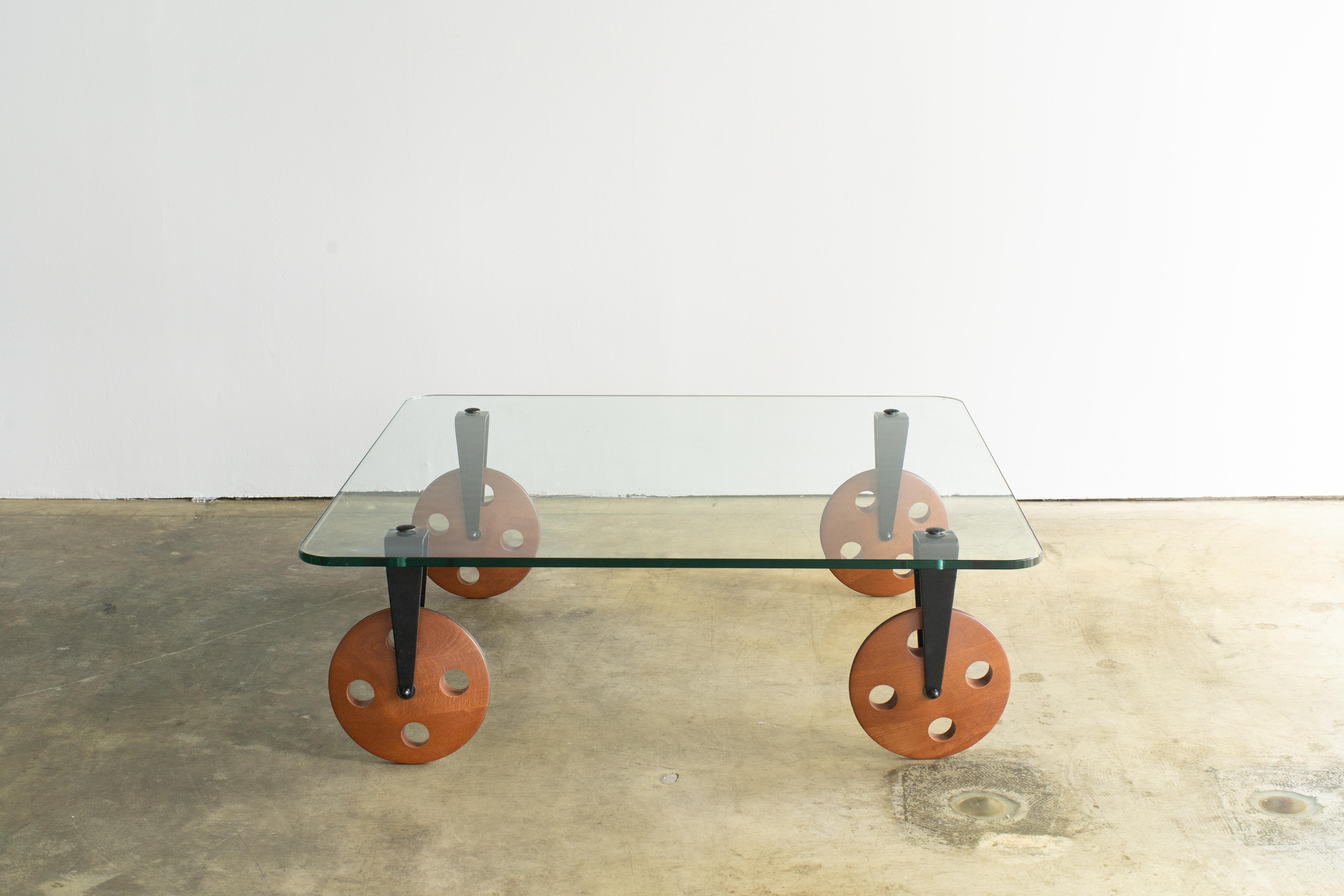 Mid-century style glass table. Similar style of Game Aulenti's table. 
Four walnut wheels and tempered glass top. Easy moving. Each wheel has rubber on its edge in order not to slip. Good condition.
 