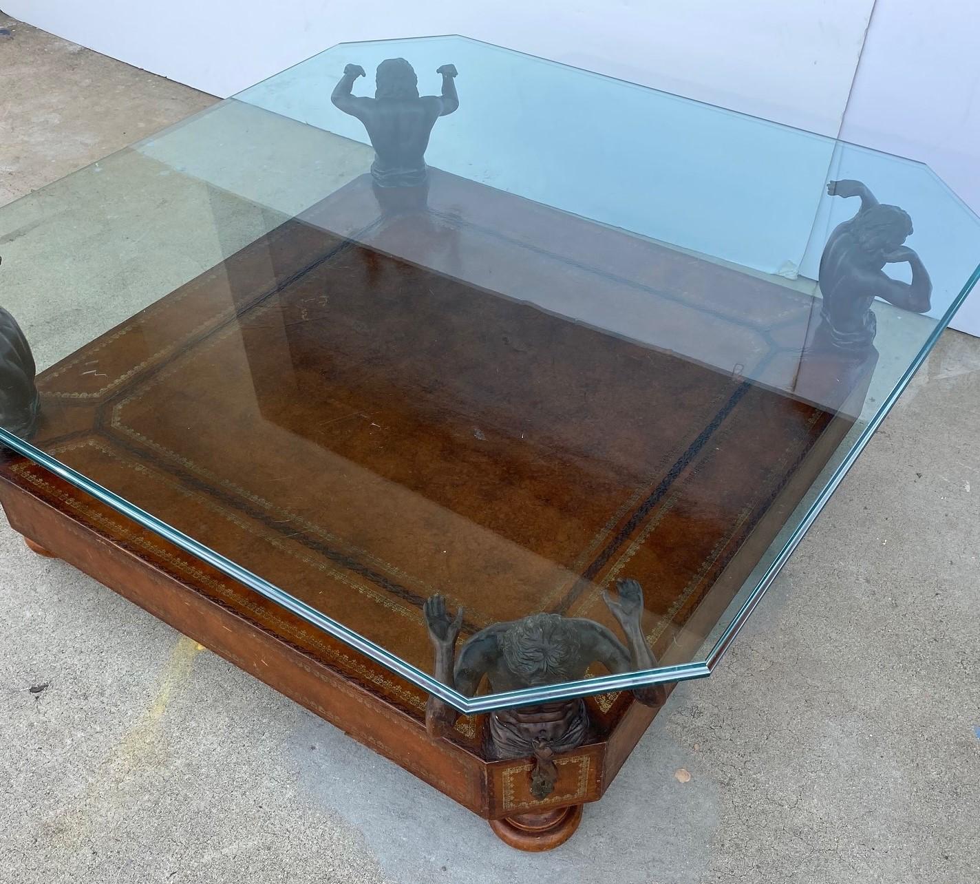 The beveled glass top sits on four bronze figures the bottom shelf is covered in embossed leather.