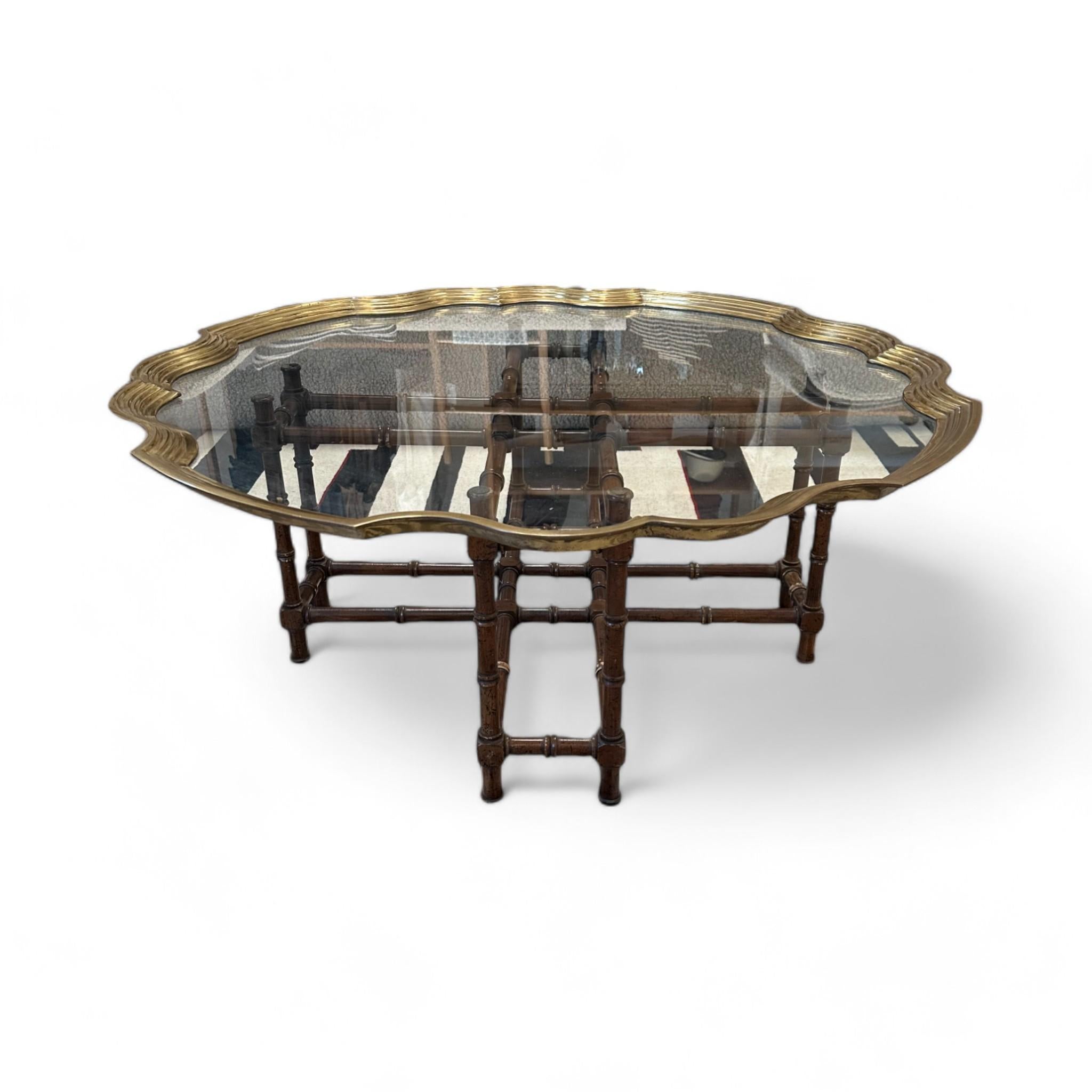 This elegant vintage coffee table features a beautifully scalloped glass top framed in brass, sitting atop a bamboo-style wooden base. The intricate combination of the rich wooden texture and reflective glass surface brings a touch of sophistication