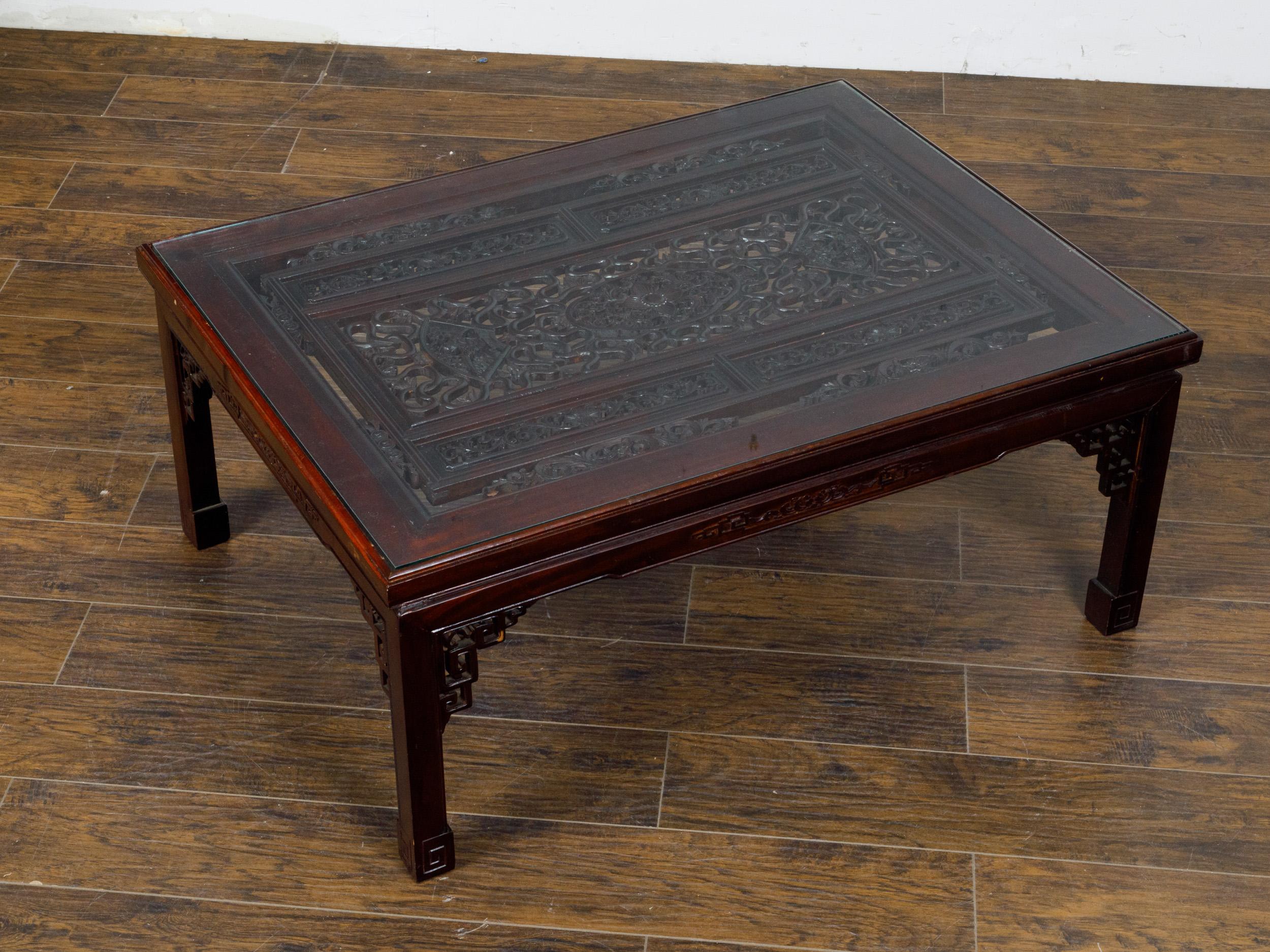 An Asian coffee table with carved fretwork top under glass and linear scrolling feet, circa 1950. This table's most captivating feature is the intricate fretwork that adorns the top, protected under a layer of clear glass, allowing one to admire the