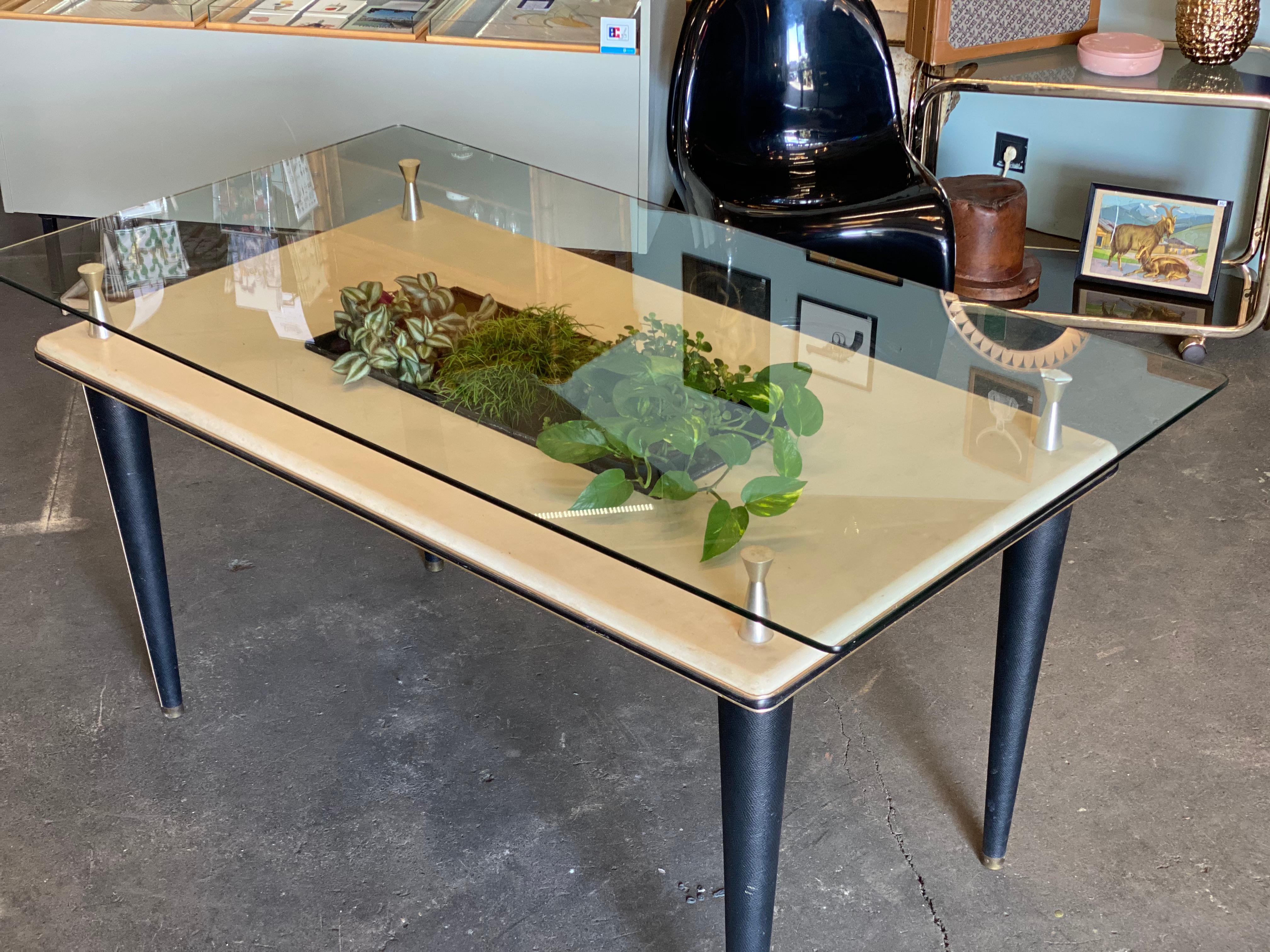 This dining table was produced in Italy during the 1950s and features a glass top with a central basin. The top and legs feature skai, as do the edges of the piece in the form of a trim around the border. The glass top and top of the frame are