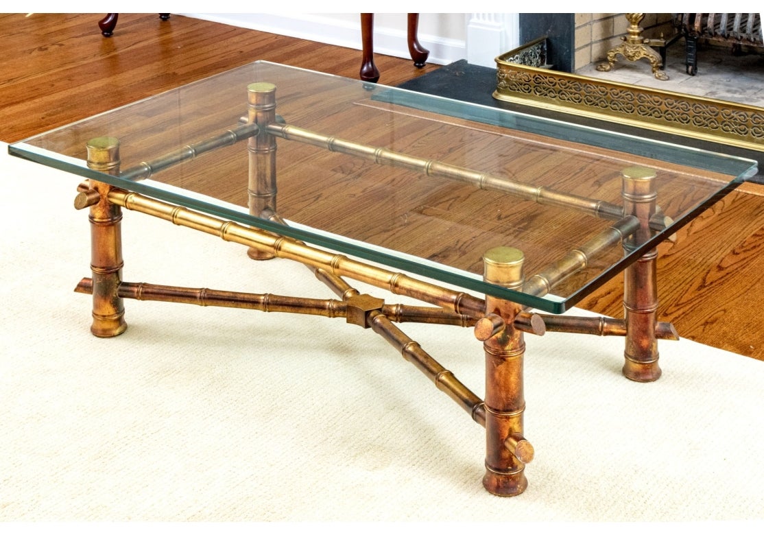 A decorative and well made cocktail table having strong lines in Bamboo form. The table features a thick rectangular glass top over a gilt faux bamboo frame with sturdy cylindrical legs supported by a top box stretcher a bottom