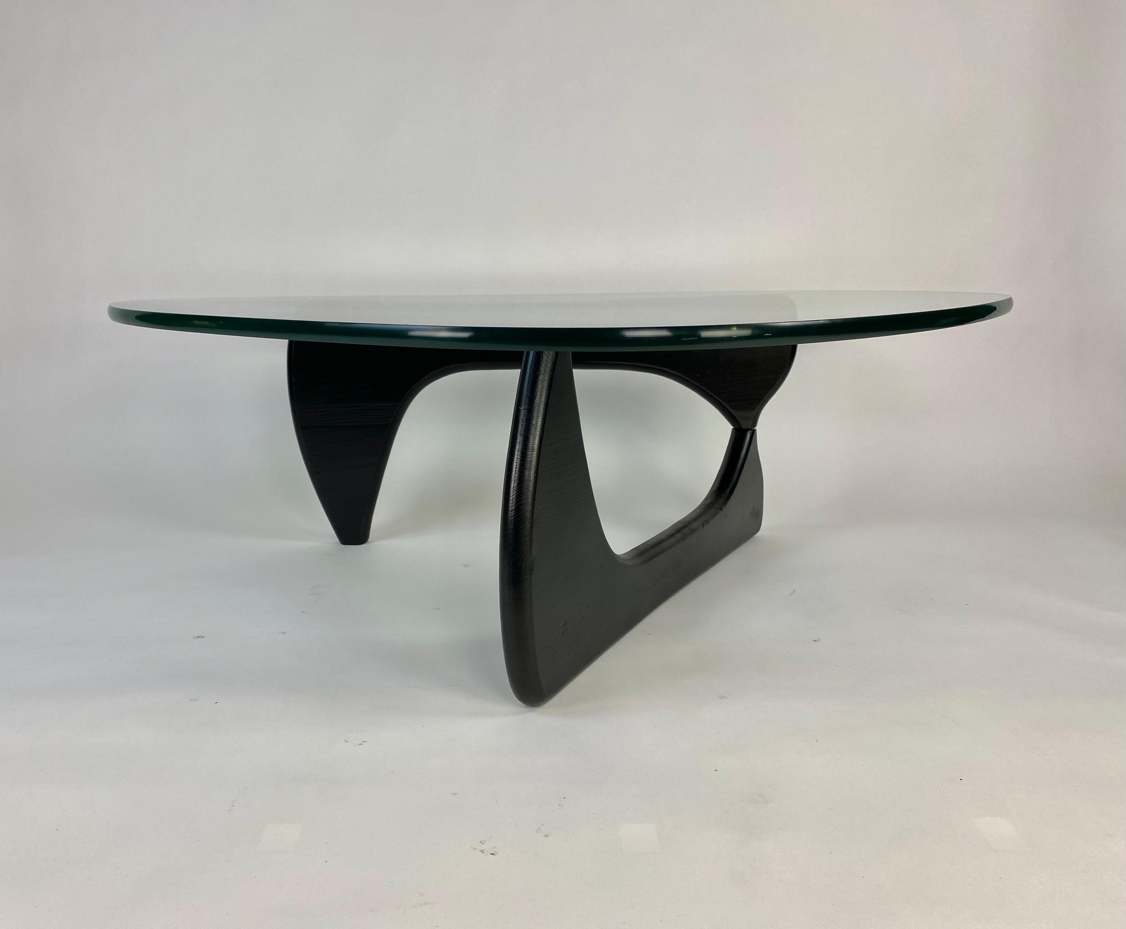 Iconic Mid-Century Modern design glass top black wood leg in the style of Isamu Noguchi. Not Herman Miller edition. The biomorphic legs interlocking via a metal pin and can be positioned in multiple orientations. No chips or cracks in glass, minor