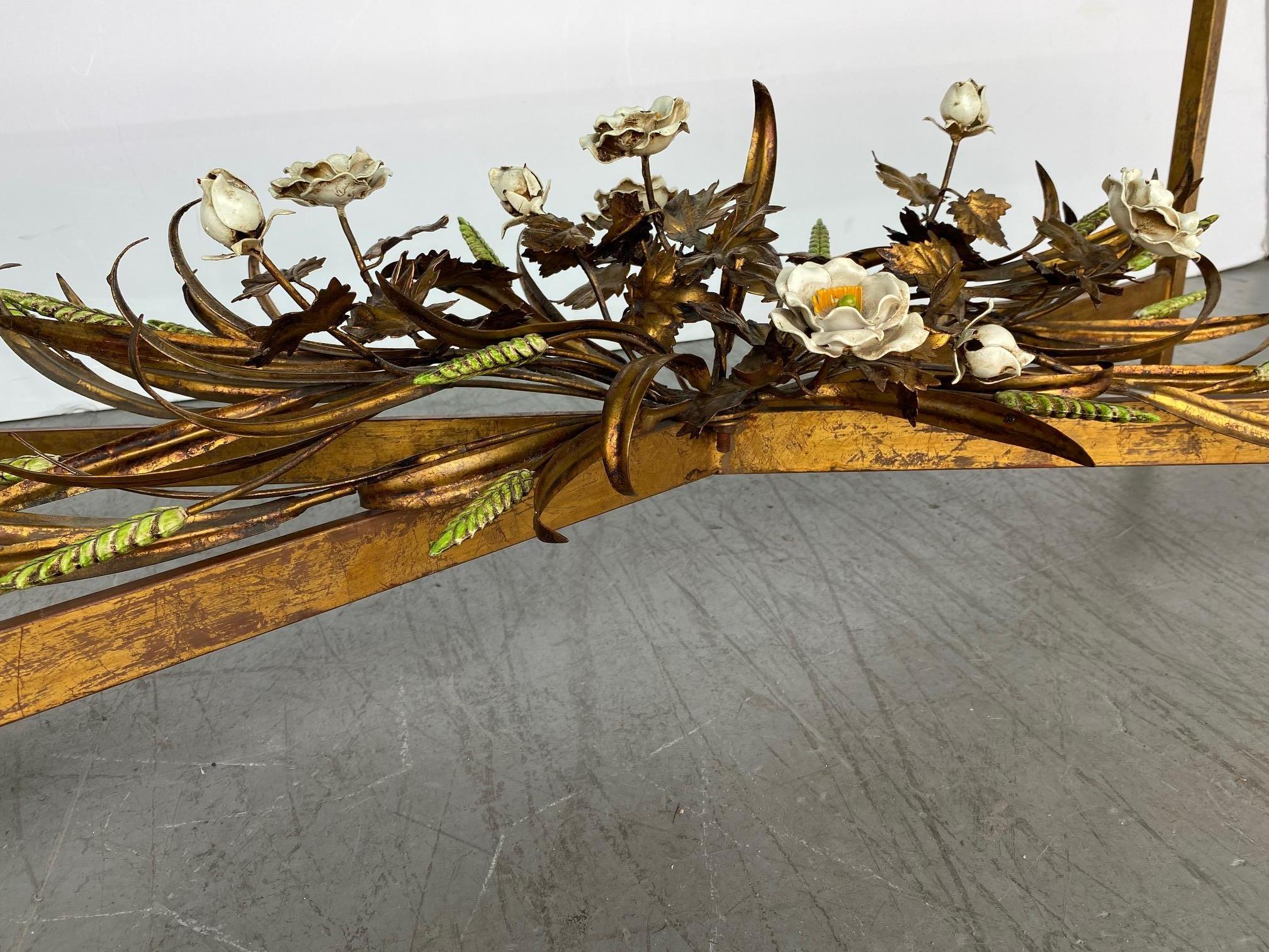A glass-top Italian coffee table. The base is gold gilded with tole and pottery flowers and leaves.