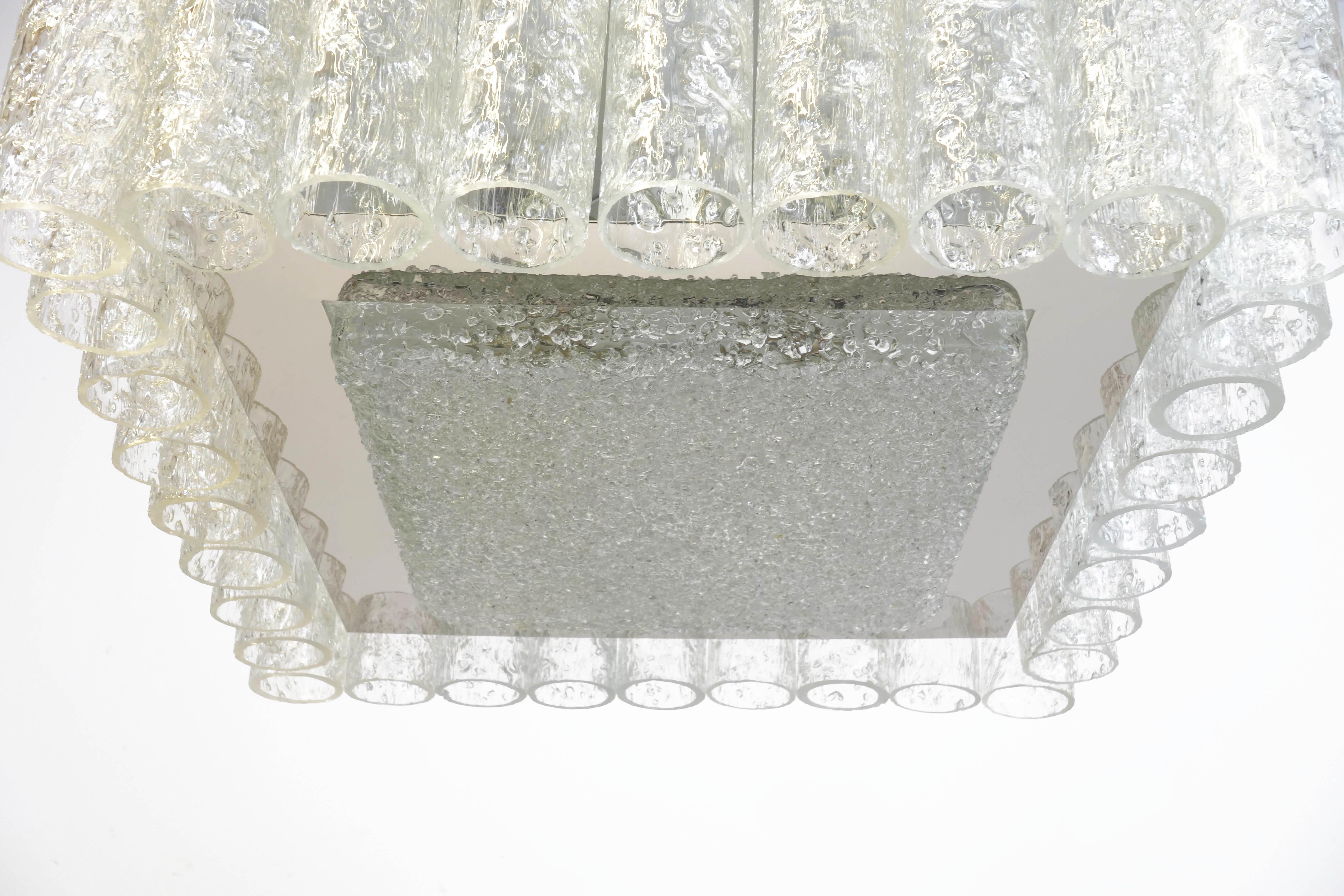 Lustre exquis en tube de verre, produit par le fabricant allemand Doria à la fin des années 1970. Son élément lumineux central est reflété par une plaque de nickel poli. L'ensemble est encadré de cylindres de verre en relief. Son caractère