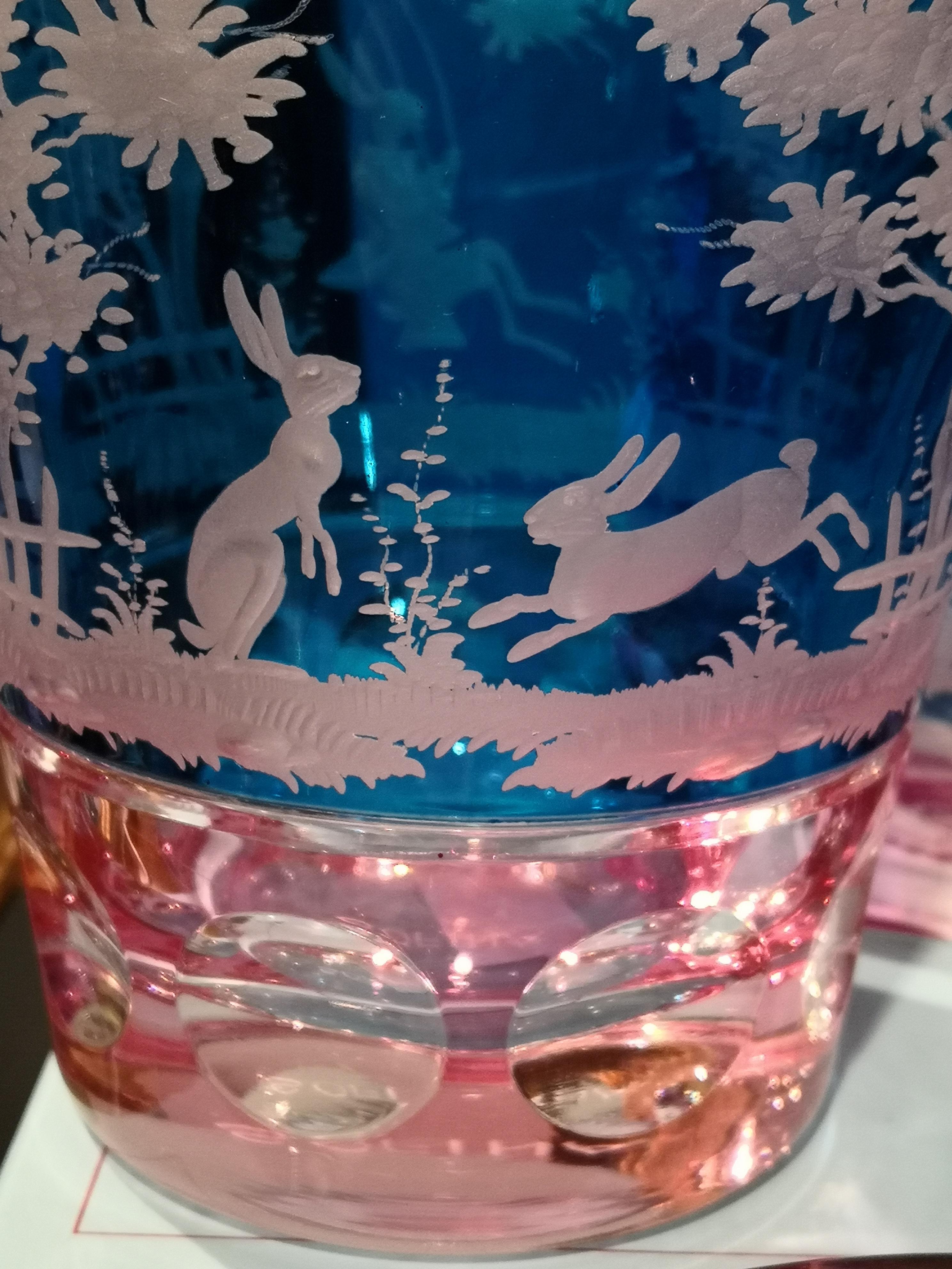 Vase aus mundgeblasenem Kristall in blauem und rosafarbenem Glas mit handgeschliffener Ostergirlande rundherum. Die Dekoration zeigt Osterhasen und Blumen rundherum. Komplett mundgeblasen und handgraviert in Bayern Deutschland. Das hier gezeigte