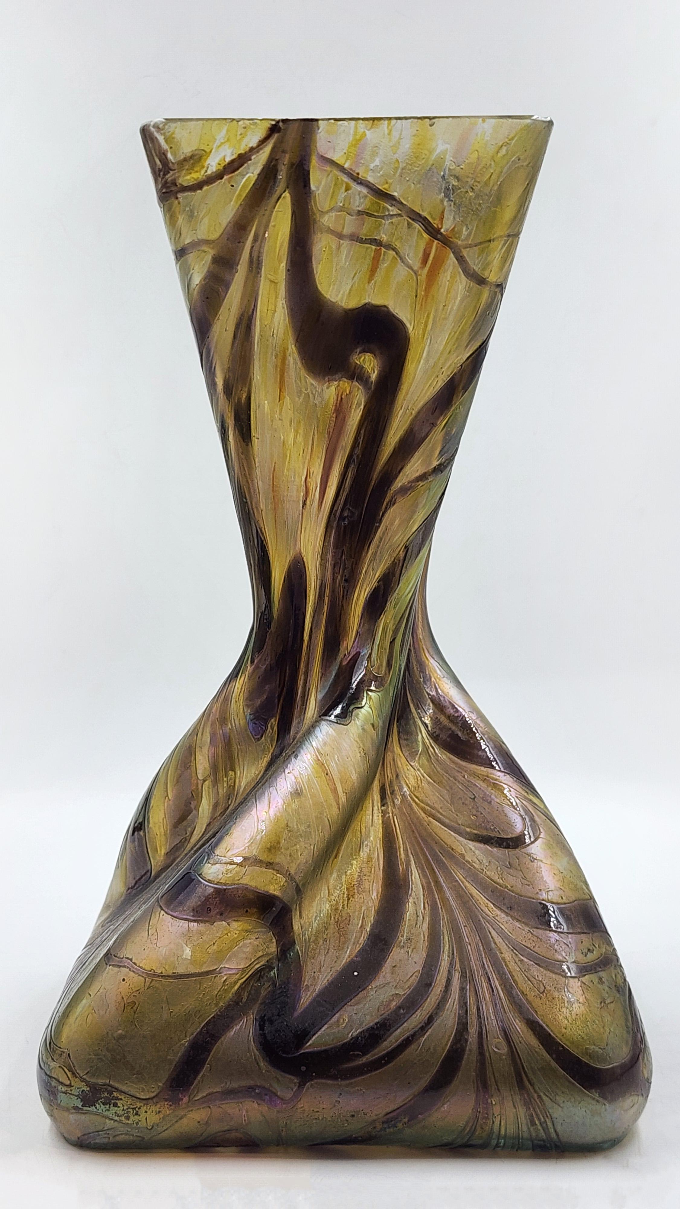 Bohemian Art Nouveau glass vase by designer Loezt
This glass vase features an asymmetrical and organic shape, with a gently twisting body, creating a dynamic silhouette that widens toward the base and narrows toward the mouth. Its color palette is
