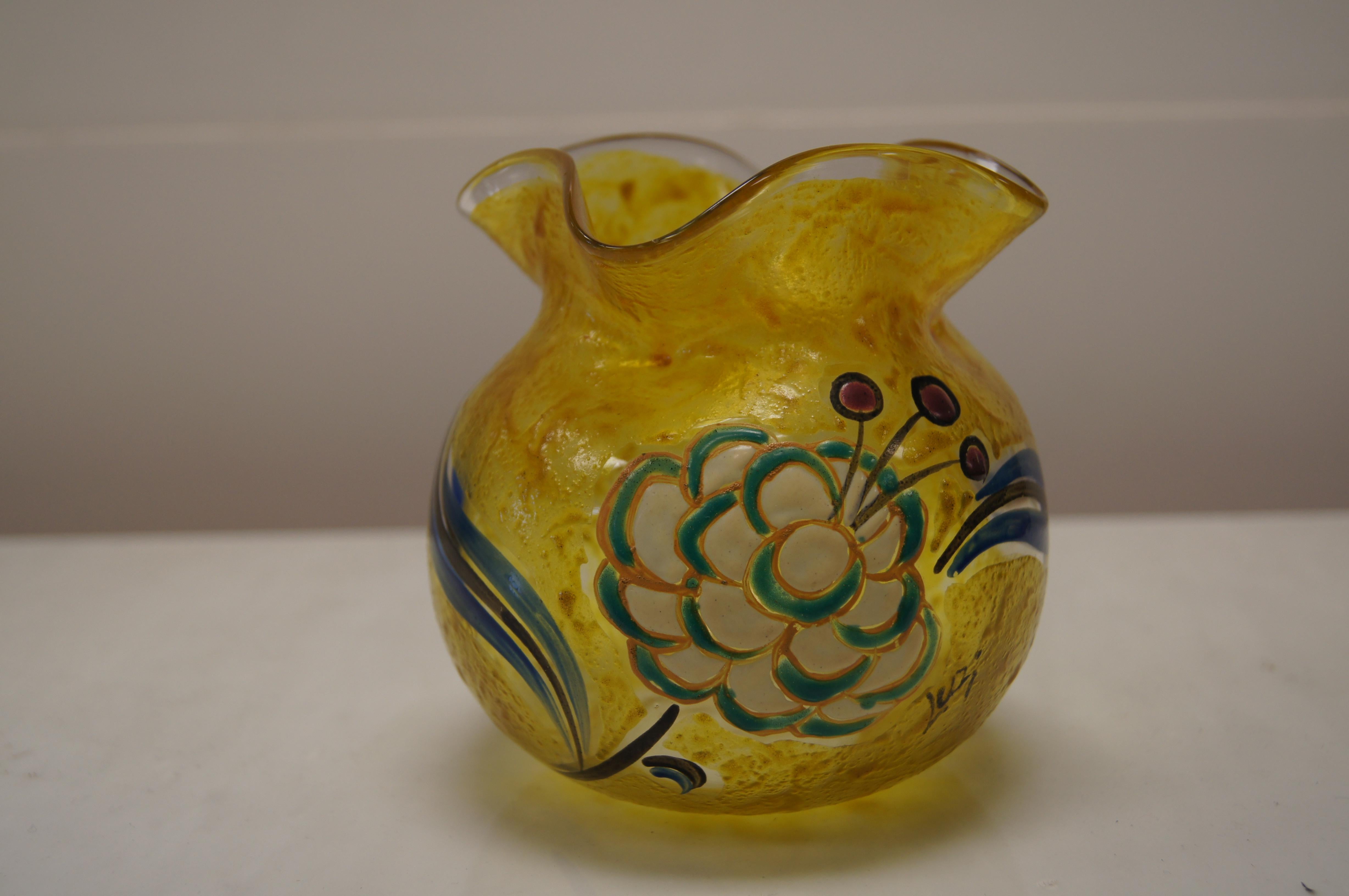 This lovely golden yellow vase from the Legras Verrerie of renowned glassmaker François-Théodore Legras features a round ball base with a fluted neck. Enameled on one side is a large flower blossom in cream, green, and blue. 

The vase is signed