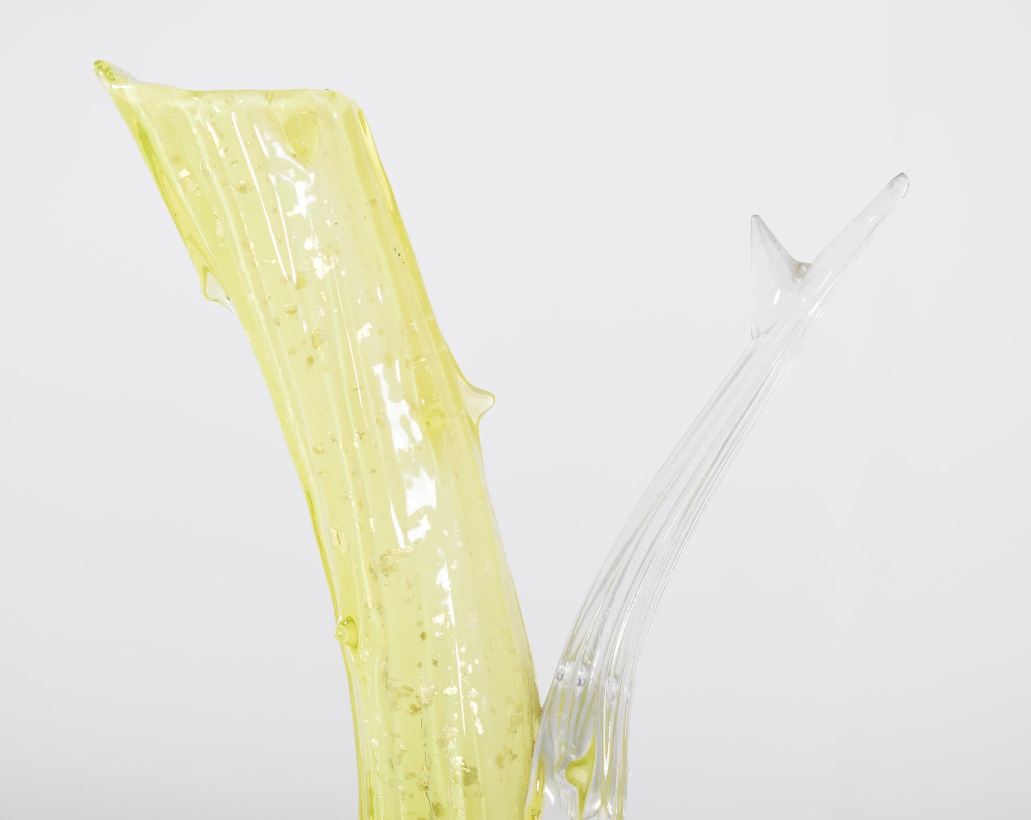 Vaso di vetro a forma di tronco. Di forma asimmetrica, il vaso rappresenta un tronco con un ramo.
La base è trasparente con dettagli in rilievo. Il corpo del vaso si sviluppa in una struttura principale giallo-verde con piccoli frammenti in rilievo