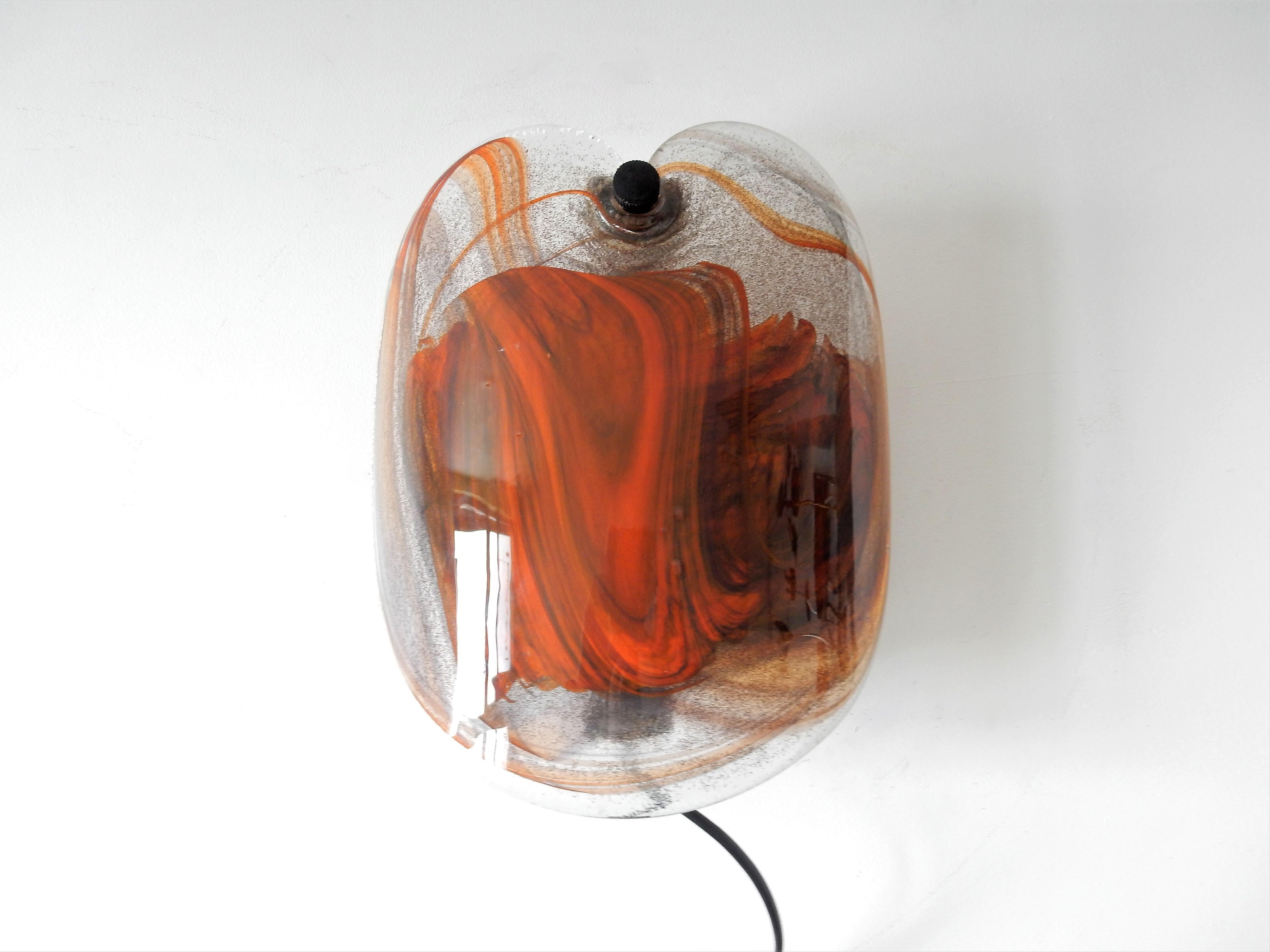 This very nice and decorative thick glass wall sconce, the 'Glasplattelampet', was designed by Per Lütken for Holmegaard in 1978. The bended glass plate is decorated with orange/brown colors inside the glass, that gives a very nice and warm glow