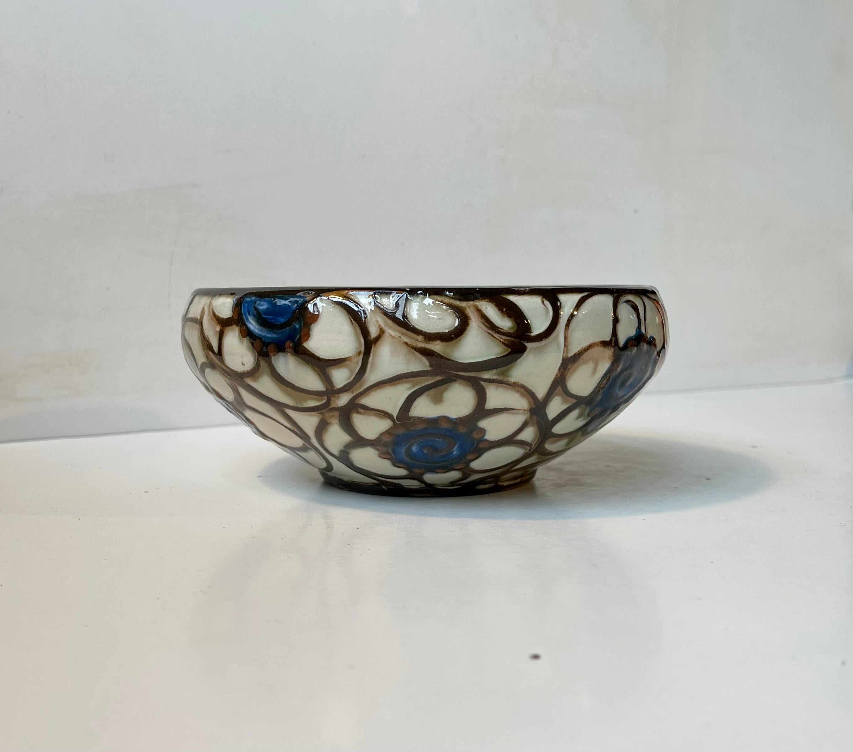 Fully glazed bowl with swirling brown stripes and blue flowers. The glaze has been applied through a cow horn - distinct Kähler Technique. Made by Herman August Kähler circa 1915-25. Signed HAK - Denmark to the base. Measurements: D: 17 cm, H: 7