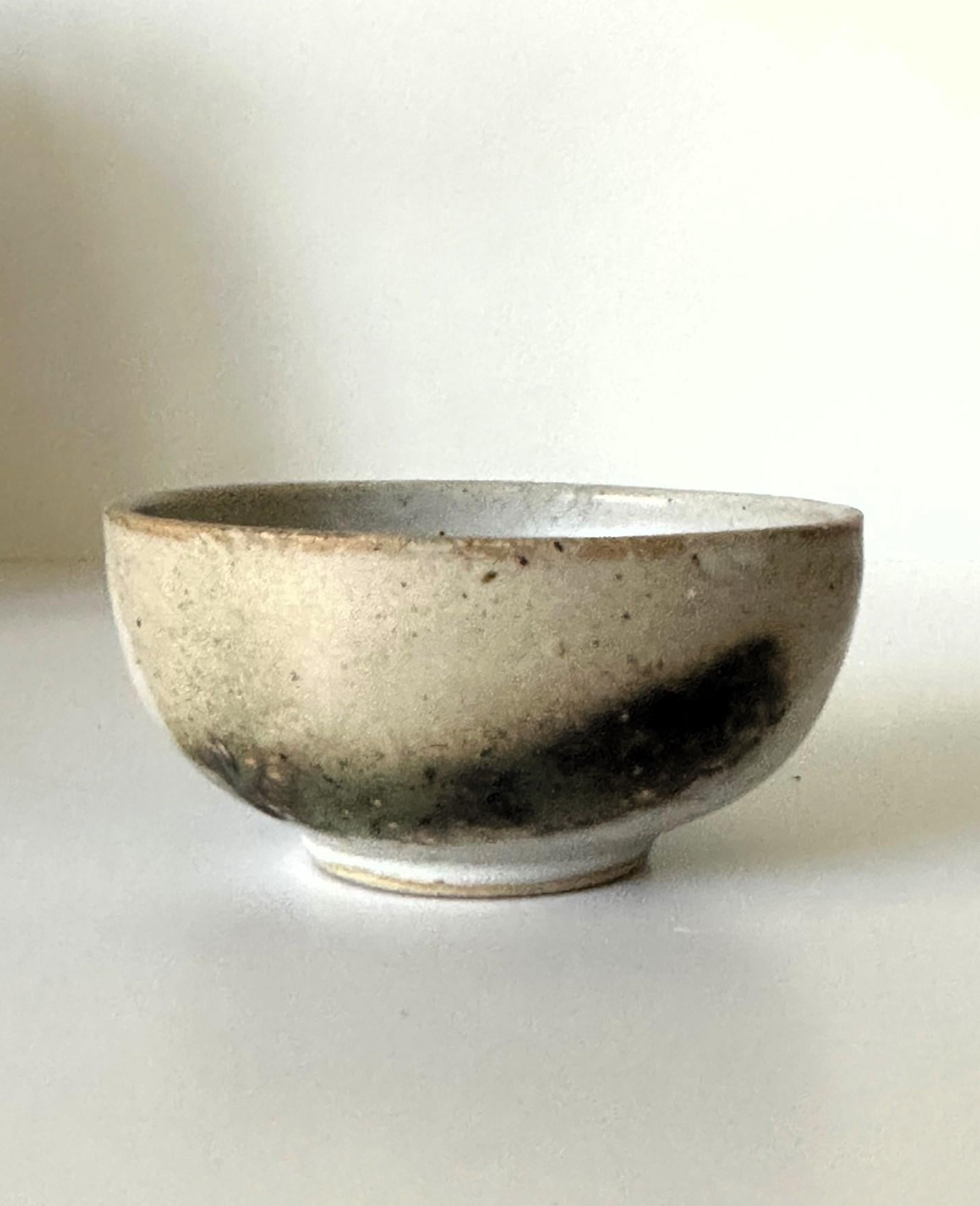 A small elegant glazed ceramic tea bowl (chawan) by Japanese American artist Toshiko Takaezu (American, 1922 - 2011). The well-balanced form is hand built and shows just a slight irregularity. The surface is covered with a white opaque glaze with a